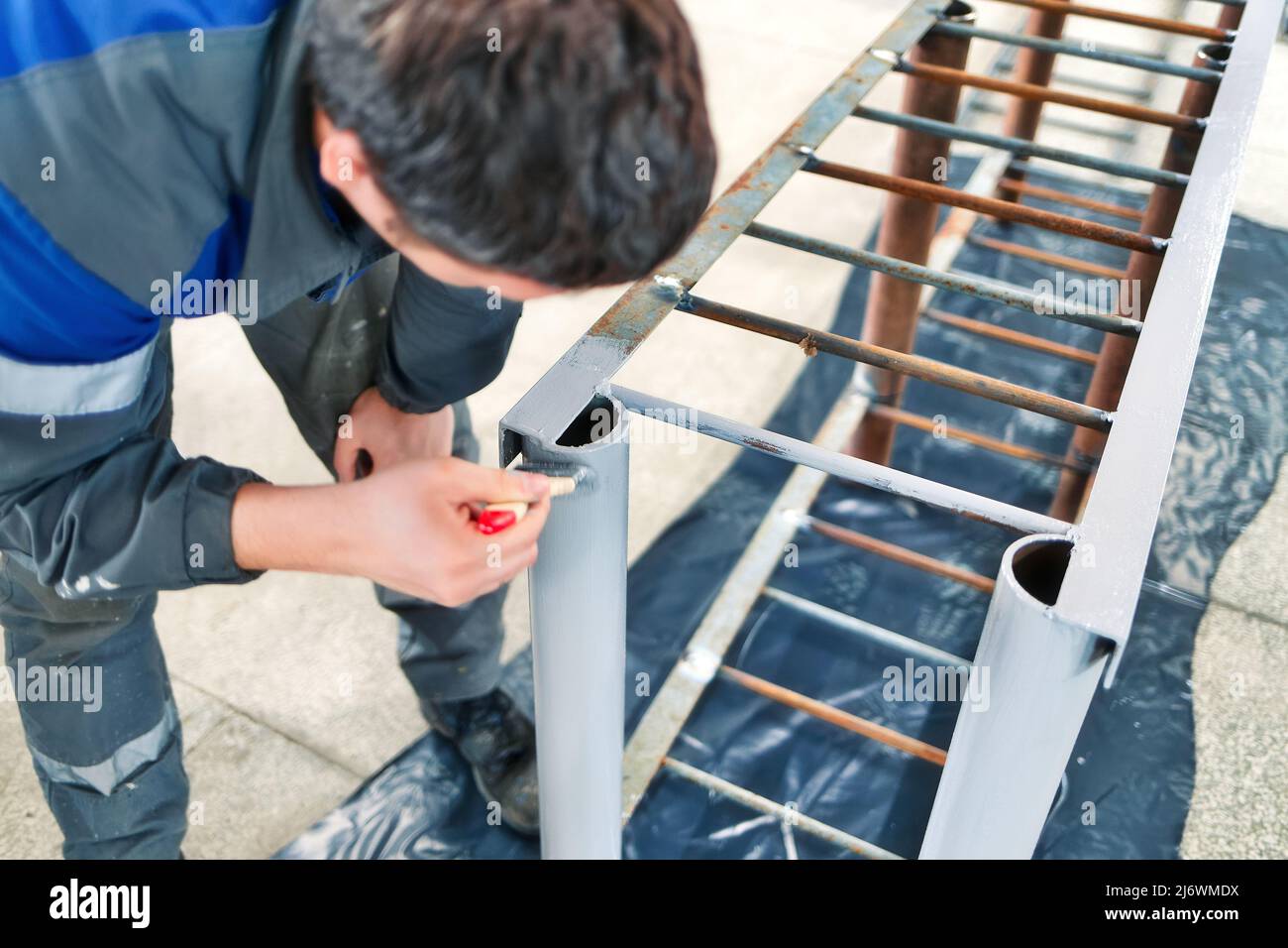 Maler von 30-40 Jahren kaukasischen Aussehen malt Metallstruktur in der Produktionshalle mit Pinsel. Echter Workflow. Stockfoto
