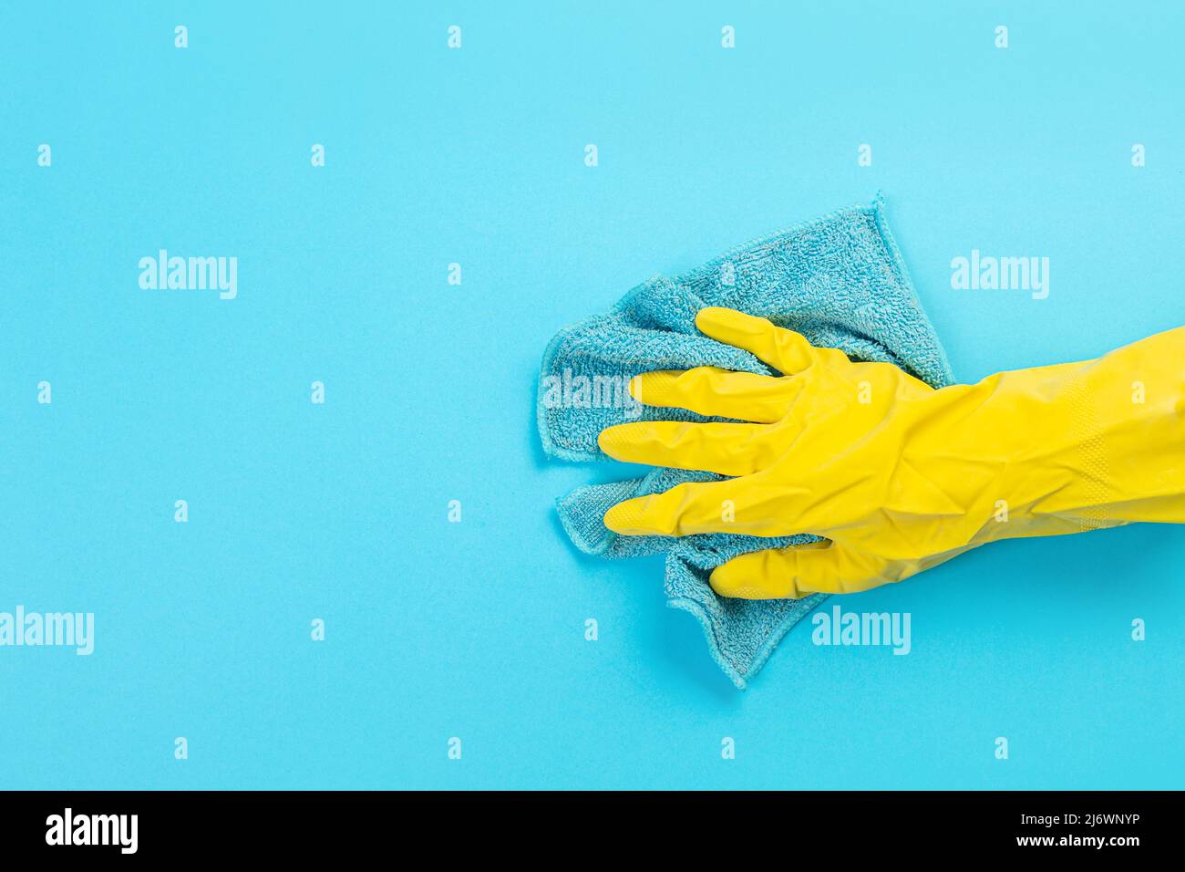 Arbeiter Hand in einem gelben Gummi-Schutzhandschuh mit einem mikrofaserblauen Tuch, das eine blaue Wand vom Staub abwischt. Ein Zimmermädchen oder eine Hausfrau kümmert sich um das Haus. Stockfoto
