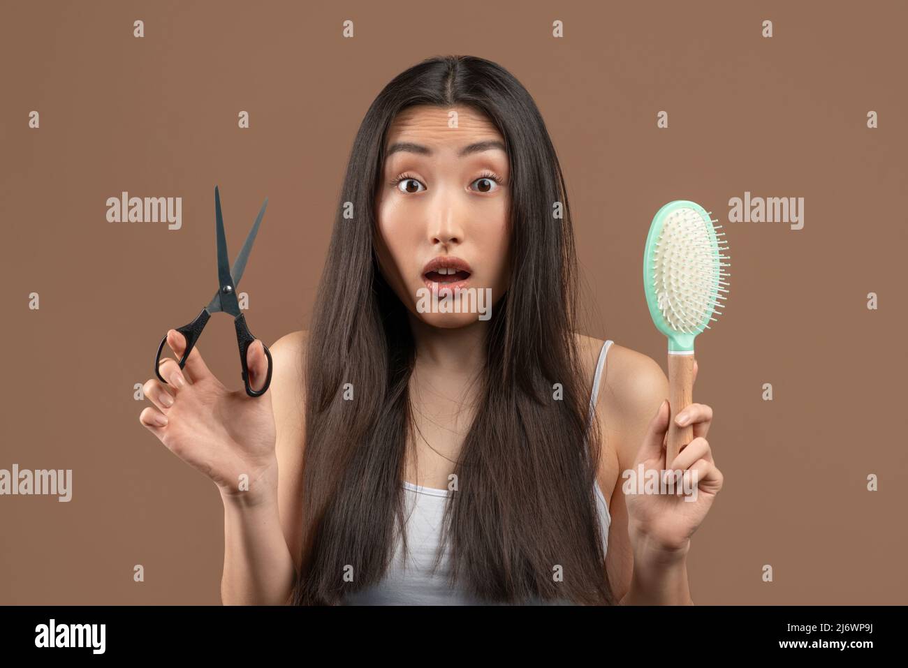 Schockierte asiatische Dame mit langen Haaren halten Kamm und Metallschere, dachte an professionelle Behandlung oder Mode Haarschnitt Stockfoto