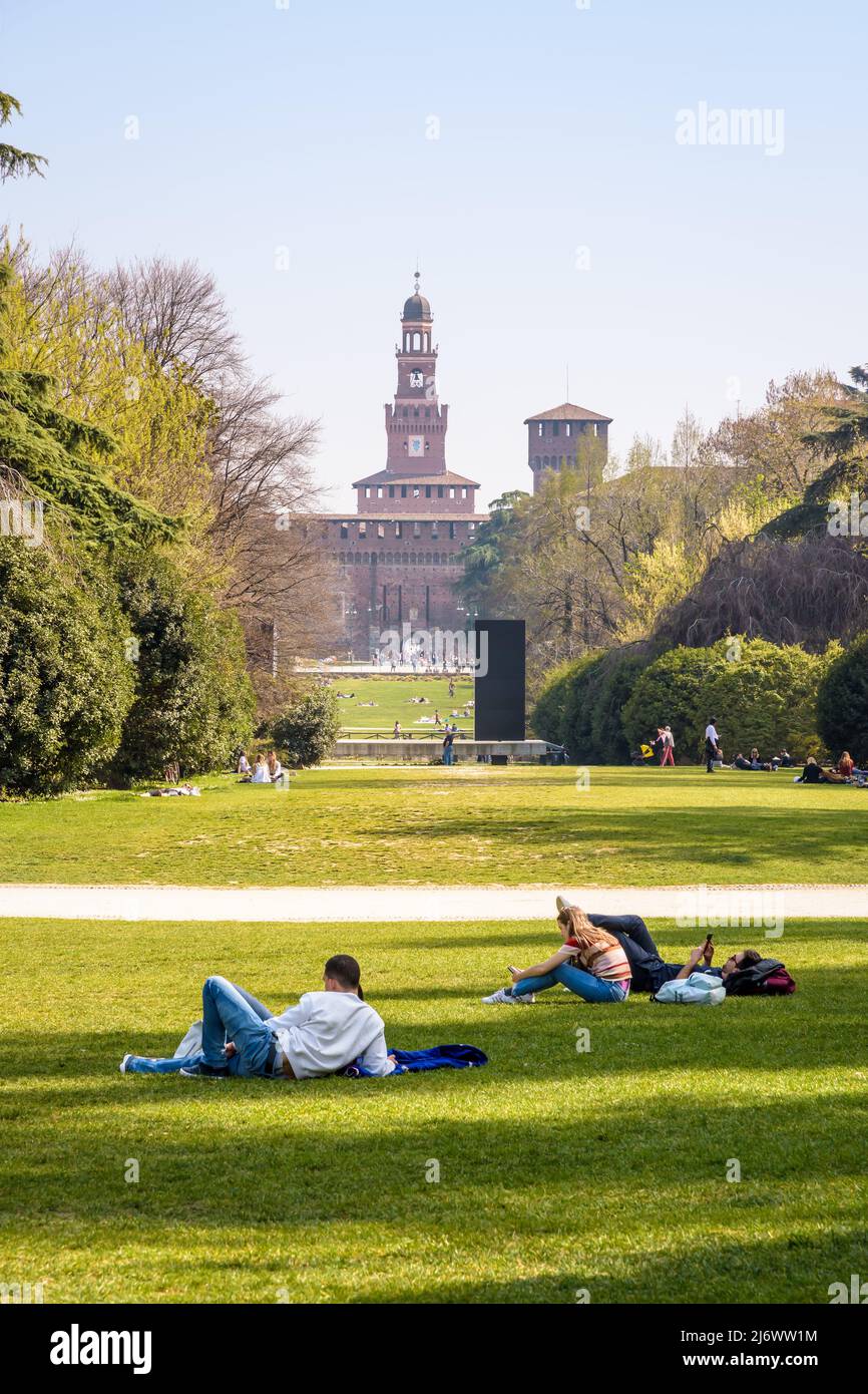Die Menschen genießen die Rasenfläche im Parco Sempione (Simplon Park) in Mailand, Italien, mit Blick auf die Türme des Castello Sforzesco (Castello Sforza). Stockfoto