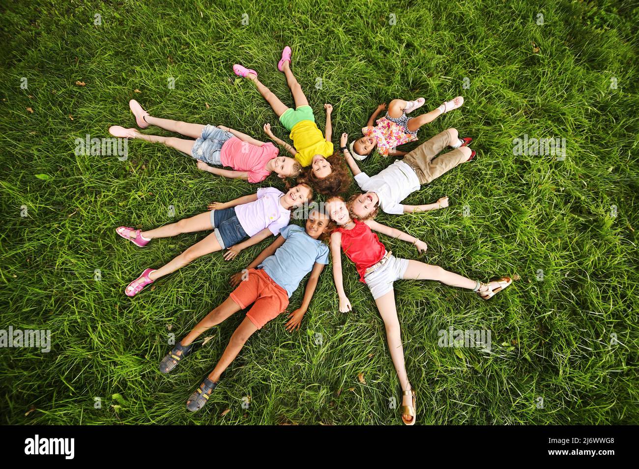 Kinder verschiedener Rassen und Nationalitäten liegen in farbenfrohen Kleidern auf dem Gras und lächeln. Kindertag Stockfoto