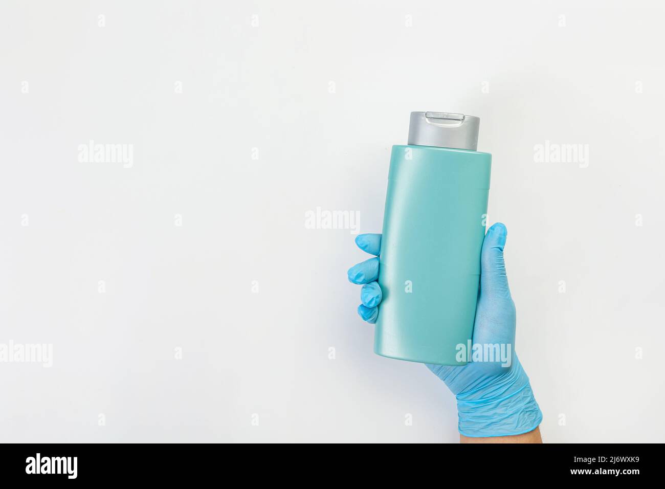 Die Hand einer Putzfrau in einem blauen Gummihandschuh hält eine Flasche Reinigungsmittel auf einem grauen Hintergrund. Reinigungsmittel für verschiedene Oberflächen in der Küche Stockfoto