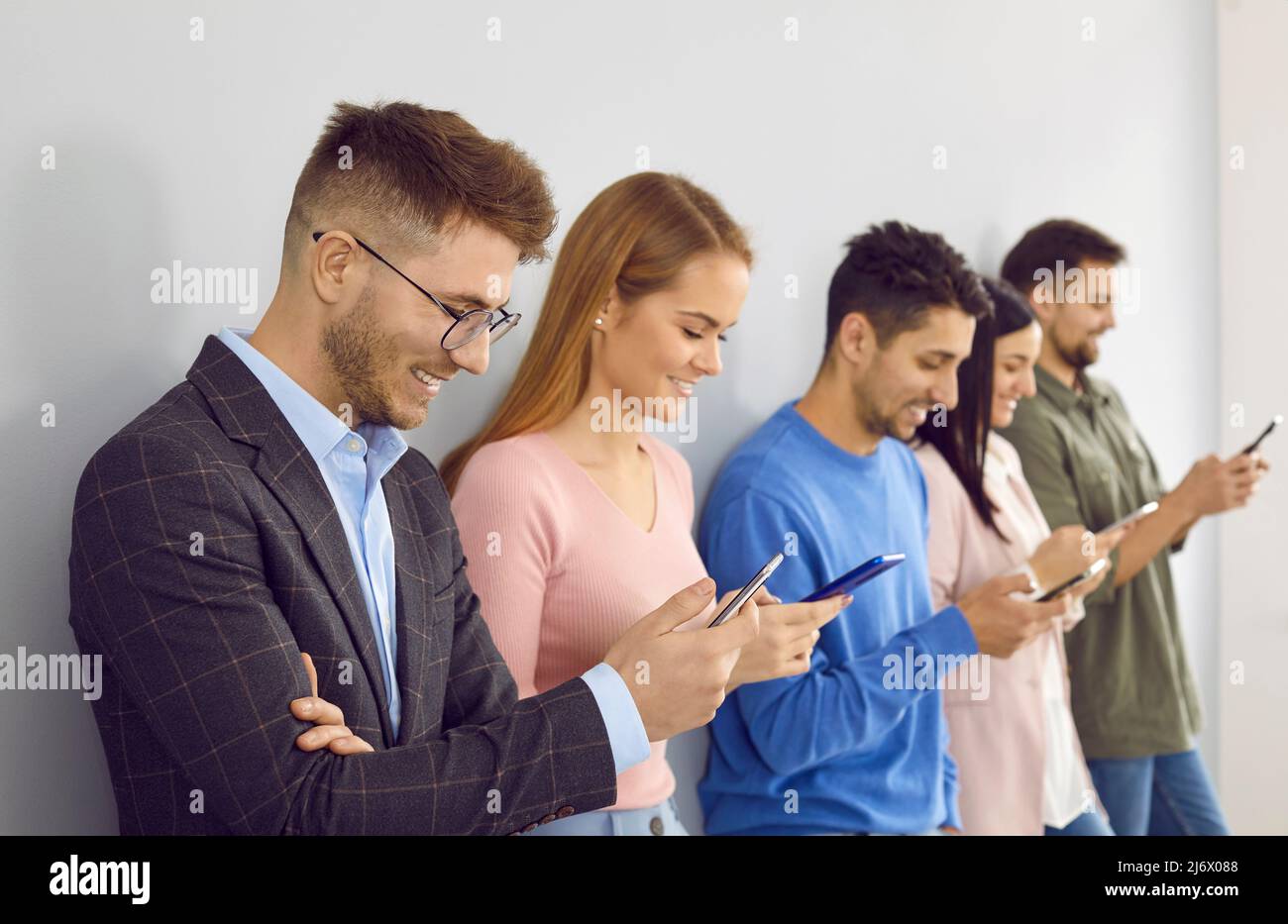 Eine Gruppe glücklicher junger Menschen, die Schlange stehen, ihr Handy benutzen und lächeln Stockfoto
