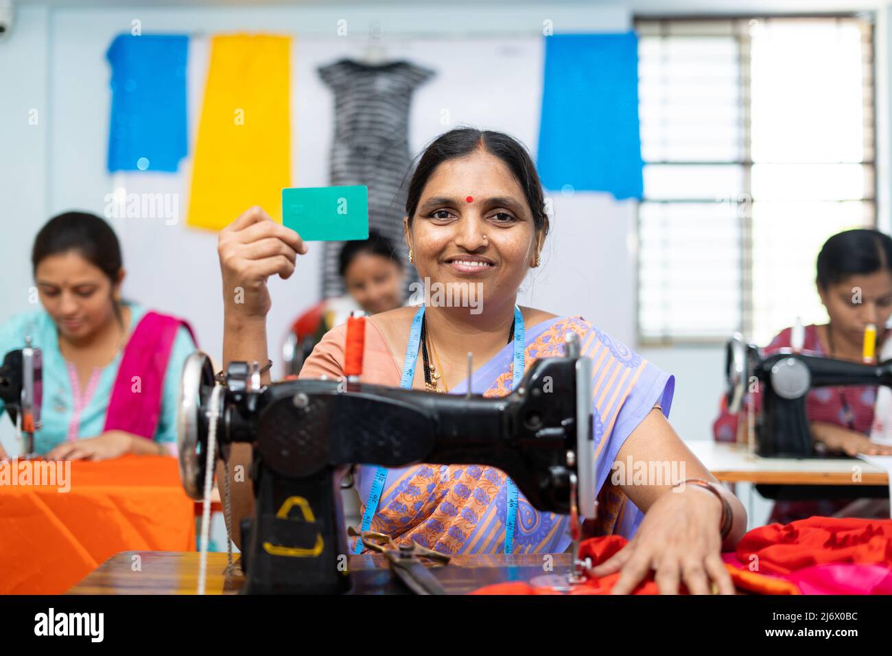 Frauen zeigen eine leere Karte auf dem grünen Bildschirm, indem sie die Kamera betrachten, während sie an Kleidungsstücken arbeiten - Konzept der mitarbeiterkennung, Werbung und Stockfoto