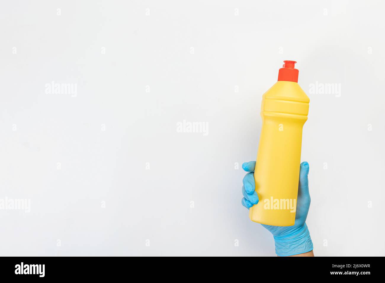 Die Hand einer Putzfrau in einem blauen Gummihandschuh hält eine Flasche Reinigungsmittel auf einem grauen Hintergrund. Reinigungsmittel für verschiedene Oberflächen in der Küche Stockfoto