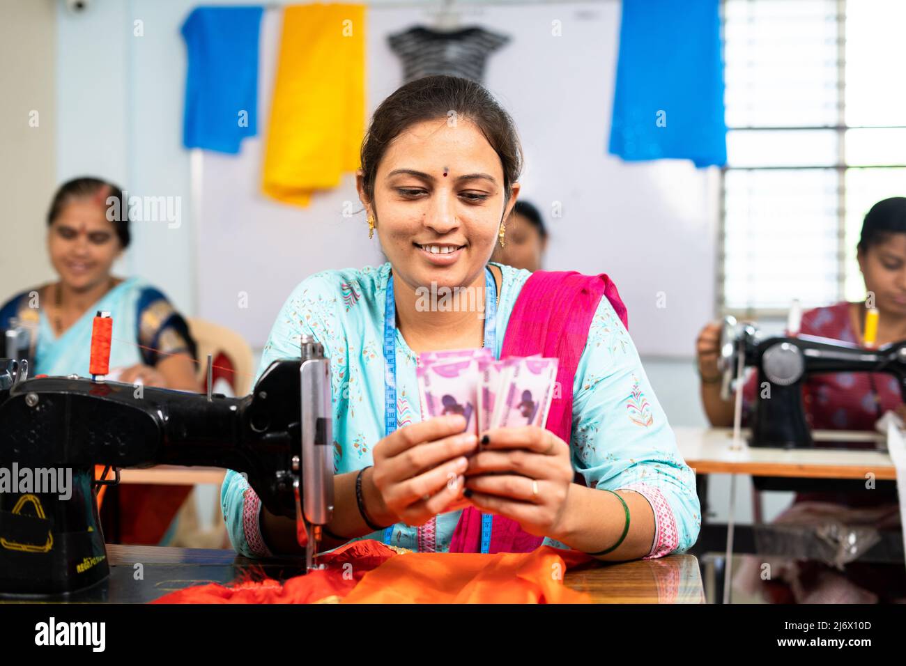 Glückliche Frauen zählen indische Währungsscheine an Kleidungsnähmaschine - Konzept des Geschäftsgewinns, Bonus und finanzielle Stockfoto
