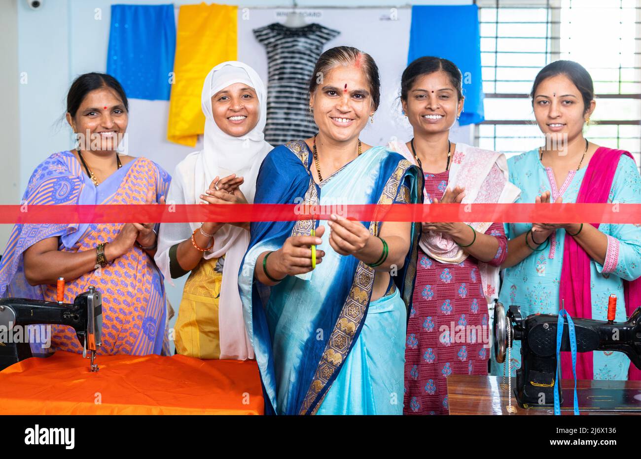 Indische Frau beginnt neue Kleider oder Schneiderei kleinen Unternehmen durch Band schneiden, während Arbeiter klatschen von hinten - Konzept der Inspiration Stockfoto