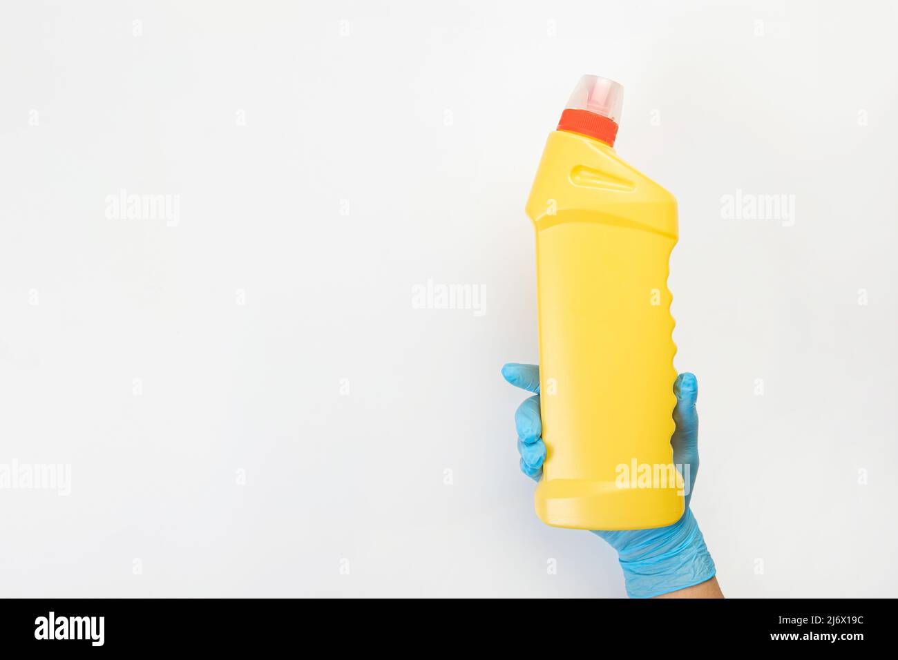 Die Hand einer Putzfrau in einem blauen Gummihandschuh hält eine Flasche Reinigungsmittel auf einem grauen Hintergrund. Reinigungsmittel für verschiedene Oberflächen in der Küche Stockfoto