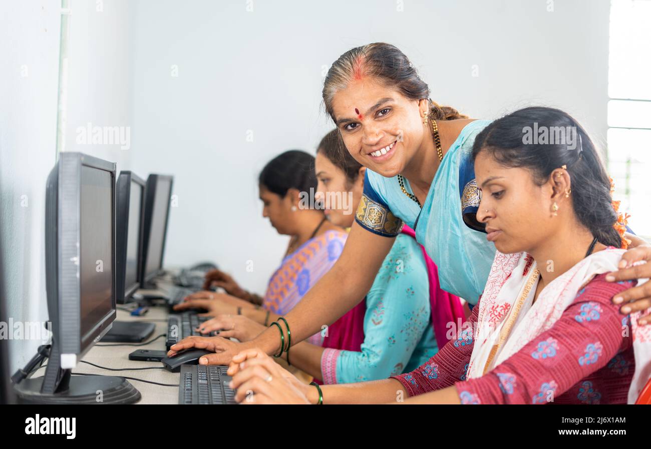 Lächelnder Lehrer, der die Kamera anschaut, während er den Frauen im Dorf Computerunterricht gibt - Konzept der Freiwilligenarbeit, Selbständigkeit und Selbständigkeit Stockfoto