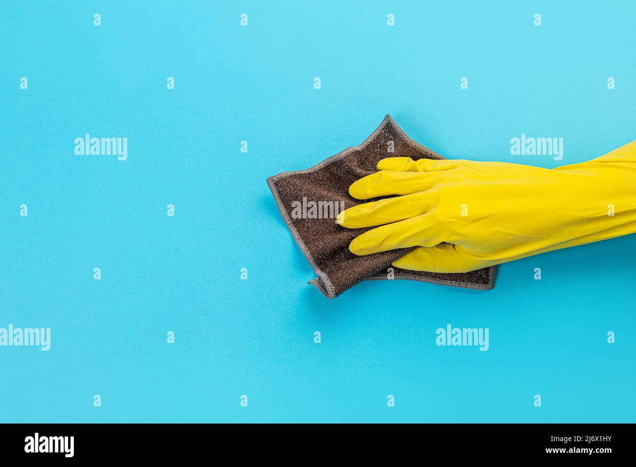 Arbeiter Hand in einem gelben Gummi-Schutzhandschuh mit einem Mikrofasertuch wischen eine blaue Wand von Staub. Ein Zimmermädchen oder eine Hausfrau kümmert sich um das Haus. Sp Stockfoto