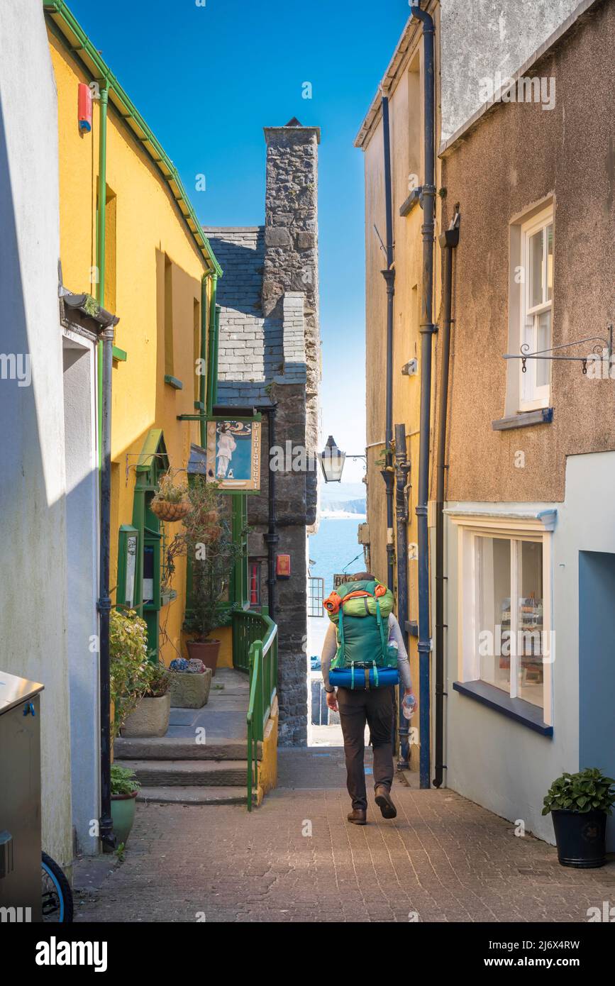 Mann reist nach Europa, Rückansicht eines Mannes mit vollem Rucksack, der alleine in einer malerischen Straße - Quay Hill - in Tenby, Pembrokeshire, Wales, läuft Stockfoto