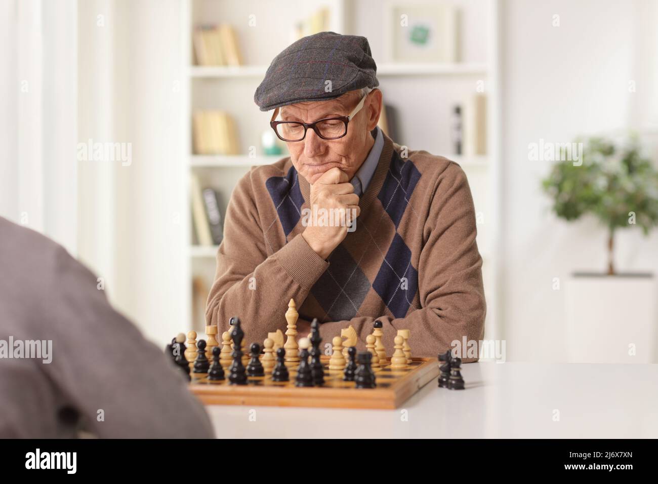 Älterer Mann, der zu Hause an einem Tisch Schach spielt Stockfoto
