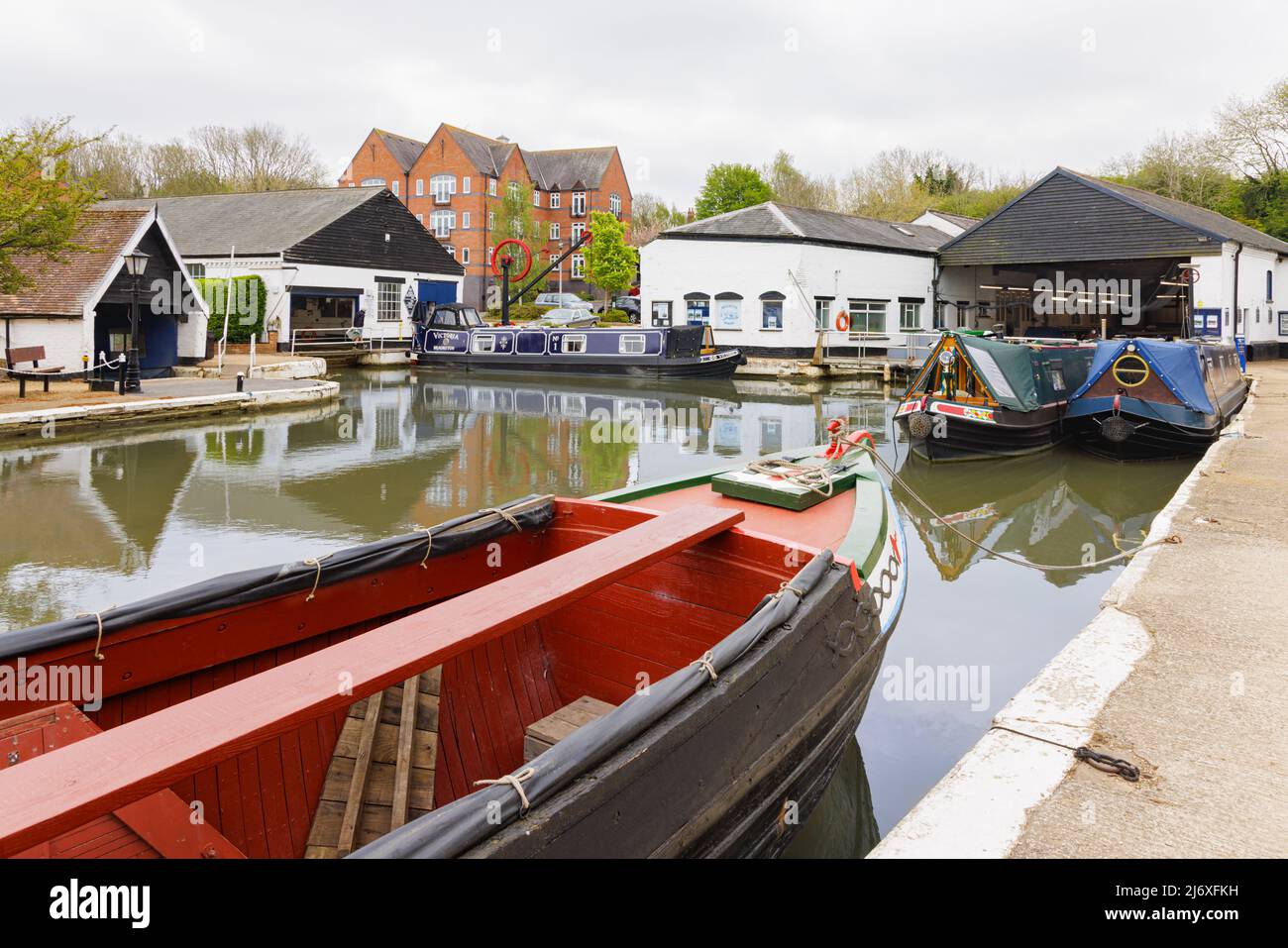 Braunston, Northamptonshire, UK, Mai 3. 2022: Narrowboats und Werkstattgebäude in Braunston Marina spiegeln sich im Wasser. Stockfoto