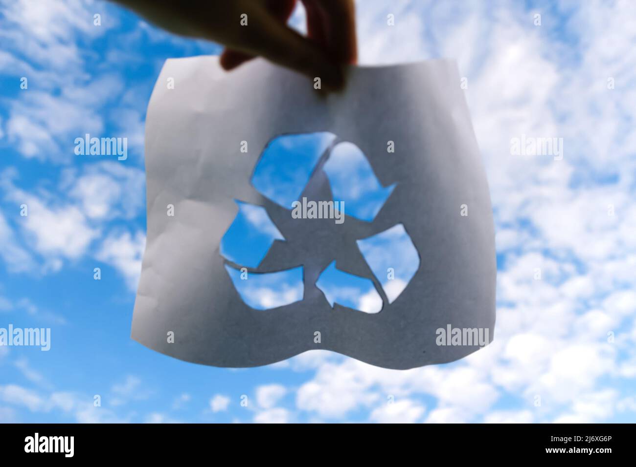 Unschärfe-Hand hält geschnittenes Papier mit dem Logo des Recyclings auf blauem Himmel Hintergrund. Recyclingkonzept. Verschmutzung des Planeten. Frieden. Nicht fokussiert. Stockfoto