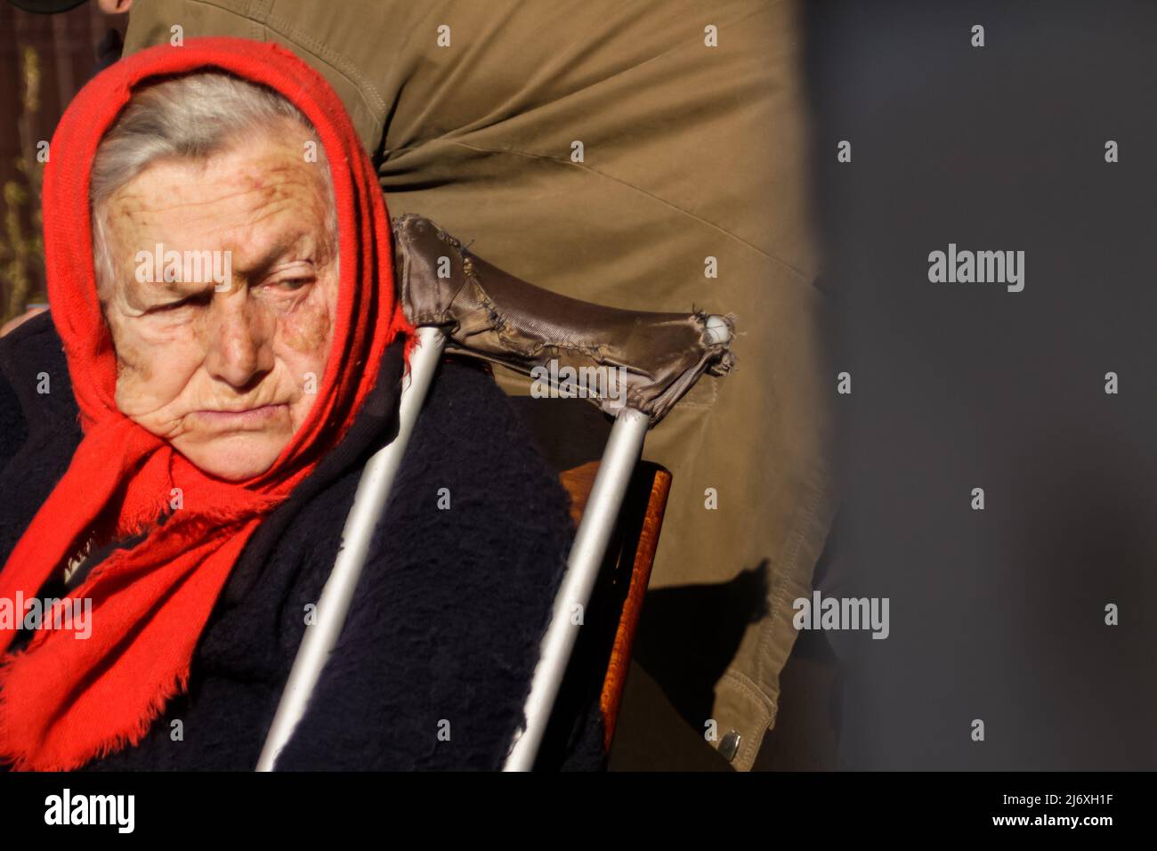 Defokussieren sie die ältere ukrainische Frau in einem roten Schal mit Krücken, die draußen sitzen. Frau 80 Jahre alt. Einzelperson. Nahaufnahme Porträt. Krank und heimatverbunden. Cop Stockfoto