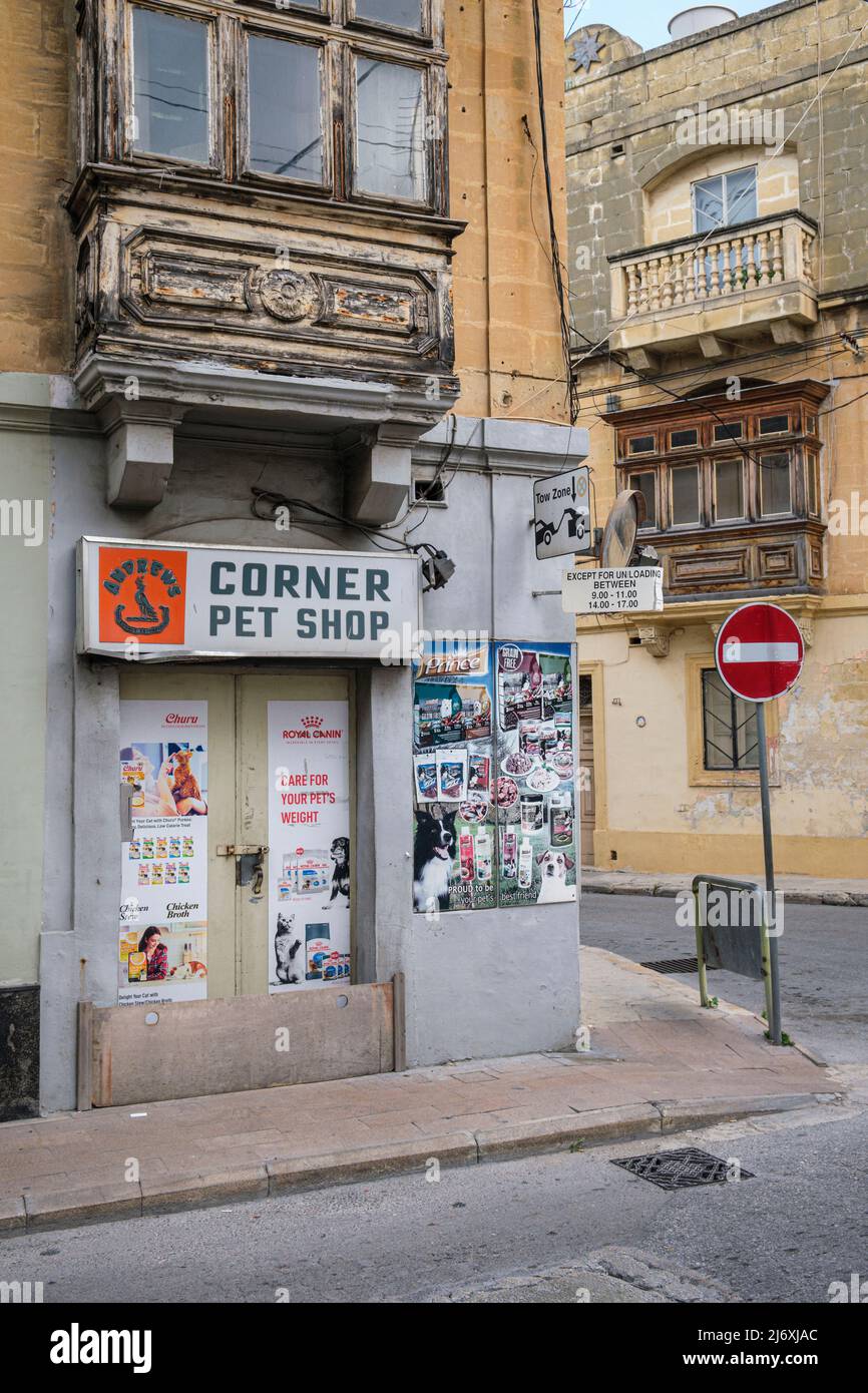 Eine Straßenecke in Tarxien mit einem Tiergeschäft und traditionellen maltesischen Balkonen auf heruntergekommenen Gebäuden, Tarxien, Malta Stockfoto