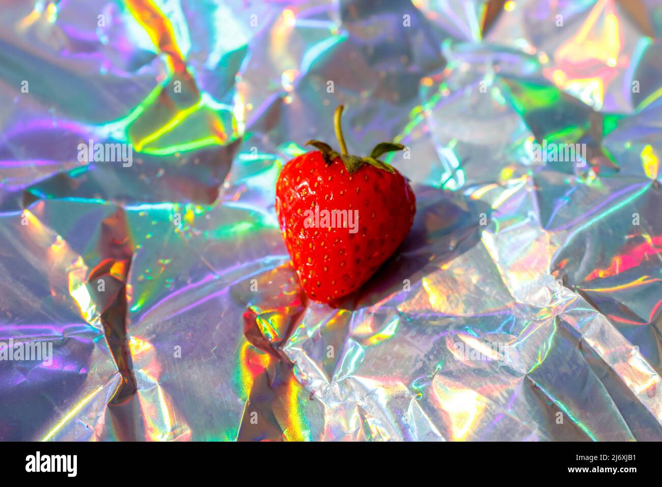 Unschärfe-Nahaufnahme einer reifen roten Erdbeere auf modernem Hologramm-Hintergrund. Früchte und Beeren. Ernte- und Erntekonzept. Organisch. Trendiger Farbverlauf. Glänzend Stockfoto