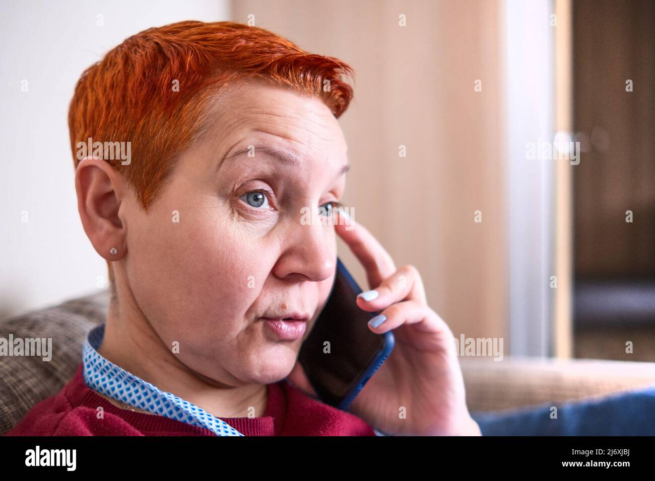 Eine Hausfrau spricht in der Küche mit einem Mobiltelefon. Das Gefühl der Überraschung, unerwartete Nachrichten Stockfoto