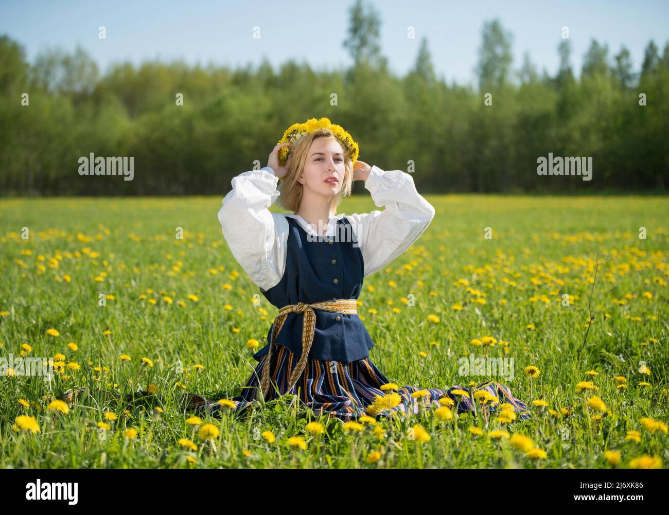 Junge Frau in Nationalkleidung mit gelbem Dandelion-Kranz im Frühlingsfeld. Frühling Stockfoto