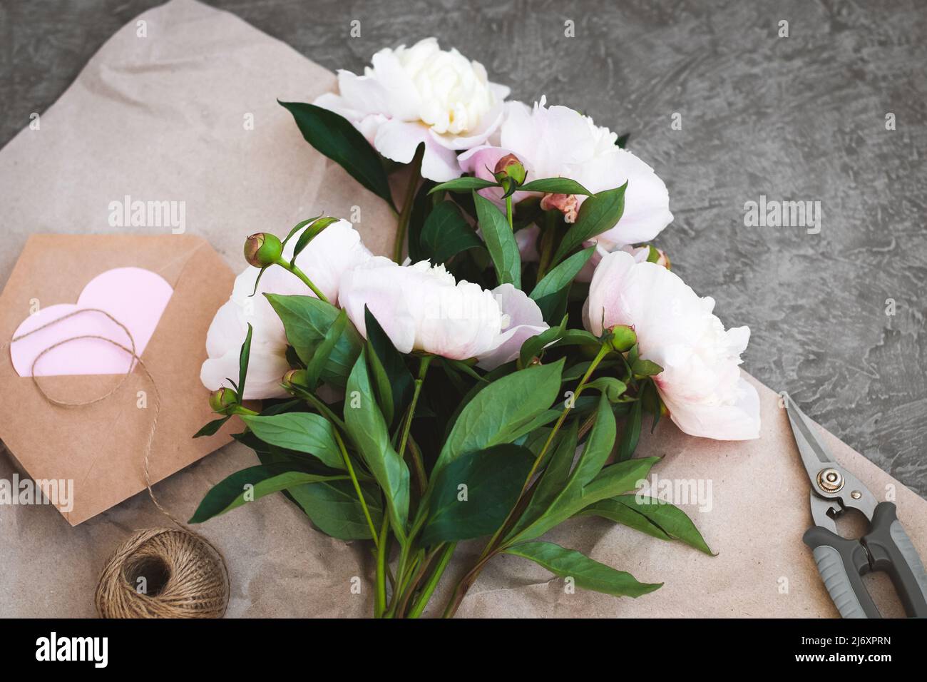Bouquet von rosa Pfingstrosen auf dem Tisch, Umschlag mit rosa Papier Herz, senden Blumen mit Liebe Stockfoto