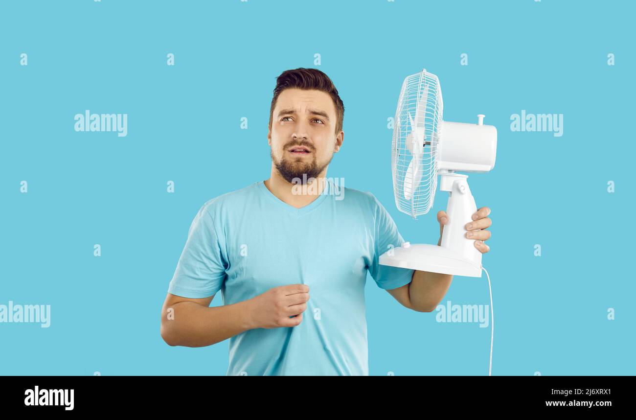 Der Mensch leidet unter Sommerhitze, fühlt sich extrem heiß an, nutzt einen elektrischen Ventilator, schwitzt aber immer noch Stockfoto