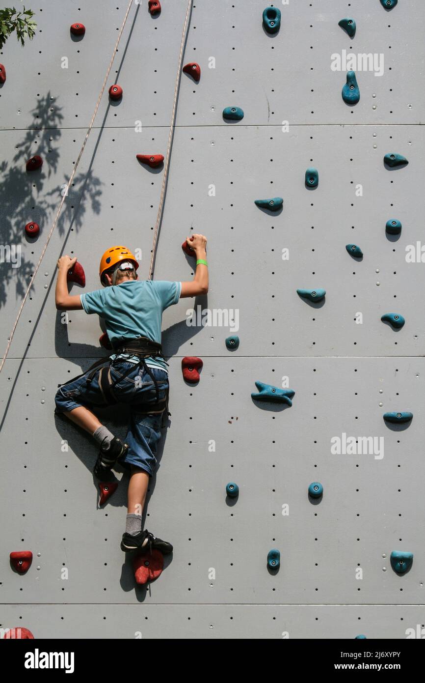 Boy klettert auf Kletterwand geschützt mit Helm und mit Seilen gesichert Stockfoto