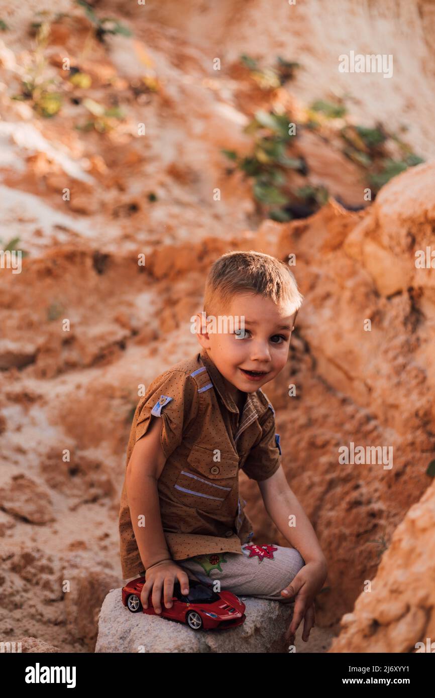 Ein kleiner Junge setzte sich auf einen Felsen im Sand. Stockfoto