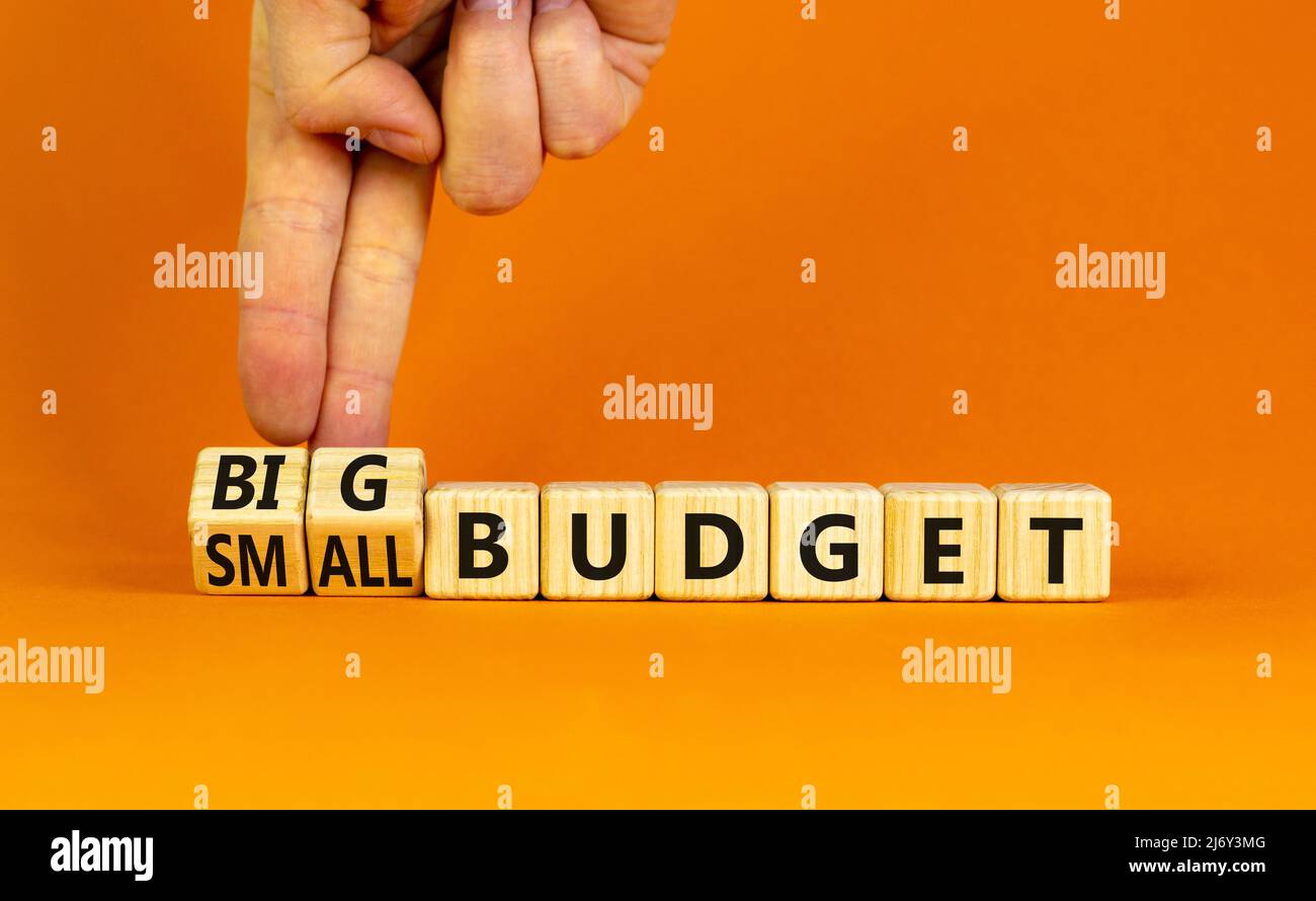 Großes oder kleines Budgetsymbol. Geschäftsmann dreht Holzwürfel und ändert Wörter kleines Budget zu großes Budget. Schöne orange Tisch orange Hintergrund, Cop Stockfoto