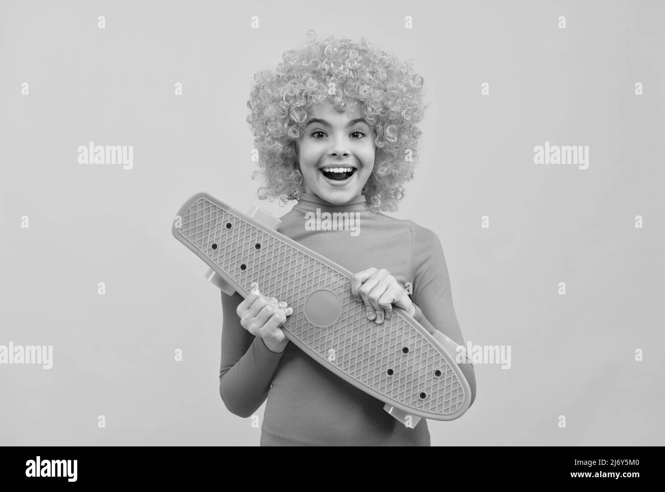 Happy cool Mädchen mit orangefarbenen Haaren in rosa Poloneck Lächeln hält Pennyboard, Skateboard Stockfoto