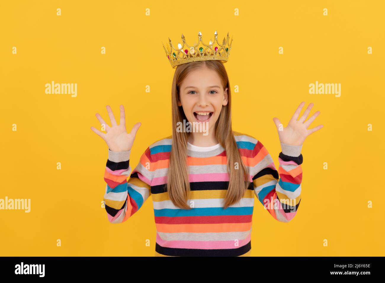 Frohes Teenager-Kind in Königskrone auf gelbem Hintergrund Stockfoto