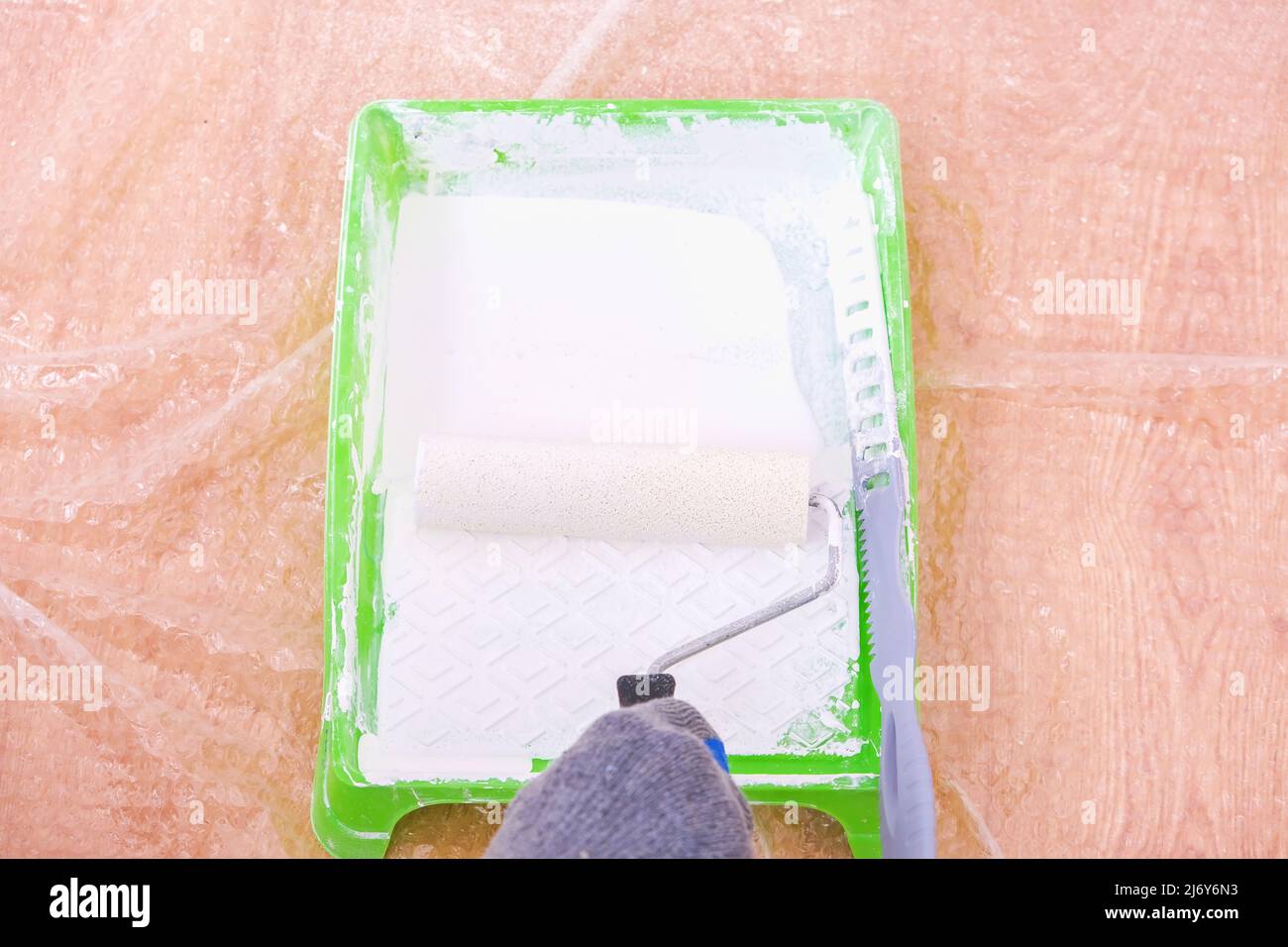 Ein Mann rollt weiße Acrylfarbe auf einer Schaumwalze in ein Farbtablett. Lackierung der Tür. Stockfoto