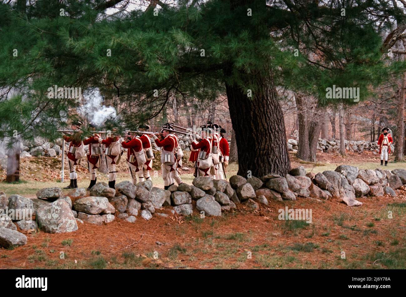 Redcoat Reenactment Charaktere feuern ihre Musketen auf Minutemen auf der Battle Road in Lexington, Massachusetts während des Patriots Day Wochenendes. Gefangen mit ana Stockfoto