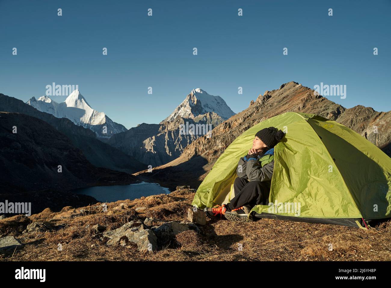 asiatische Frau Camper sitzt im Zelt genießen die frühen Morgensonne mit geschlossenen Augen im yading Nationalpark, landkreis daocheng, sichuan provi Stockfoto