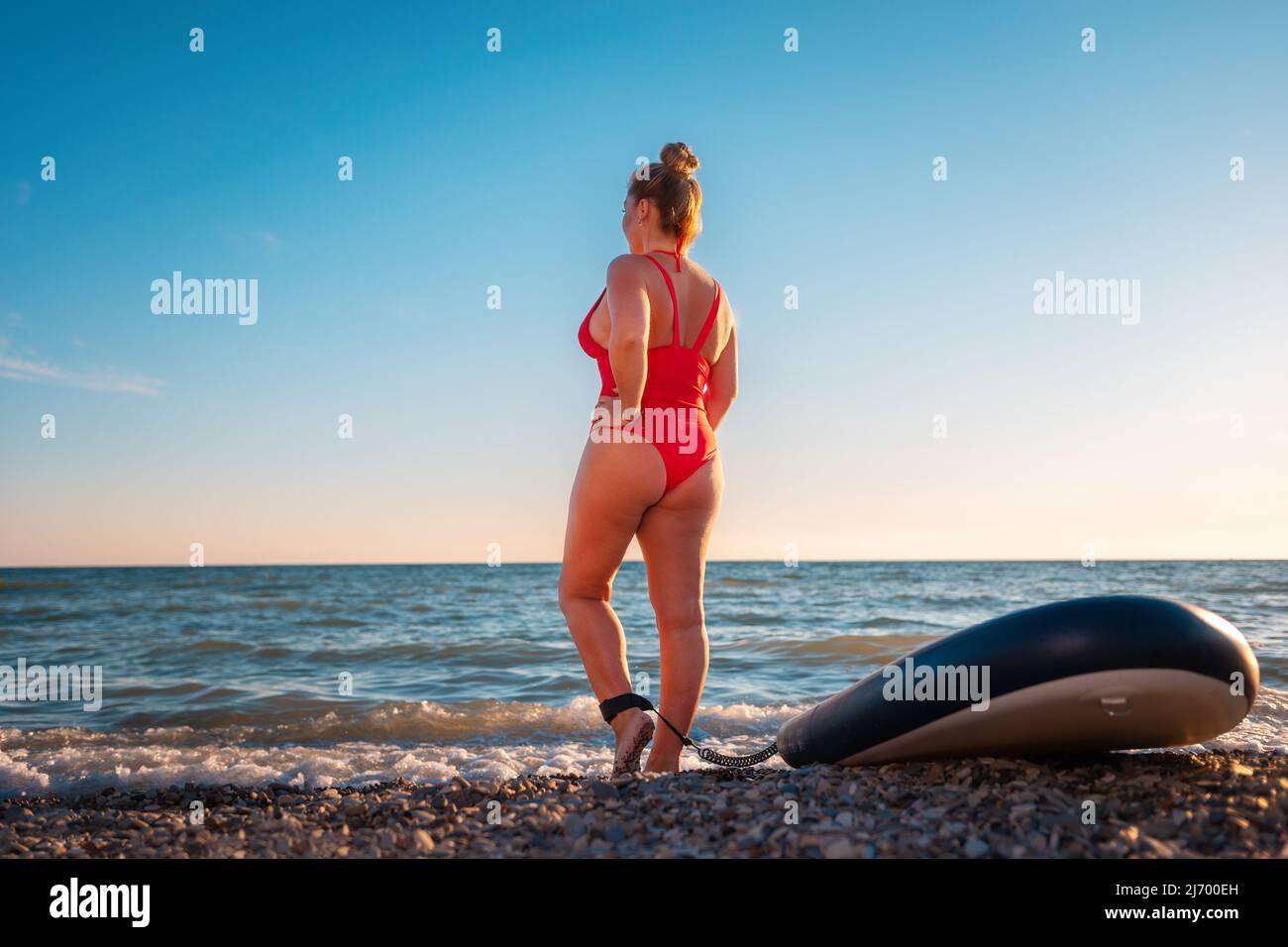 Plump Erwachsenen schöne Frau in roten Badeanzug posiert mit einem schwanzt. Rückansicht unten. Im Hintergrund ist der Himmel das Meer. Das Konzept des Sports Stockfoto