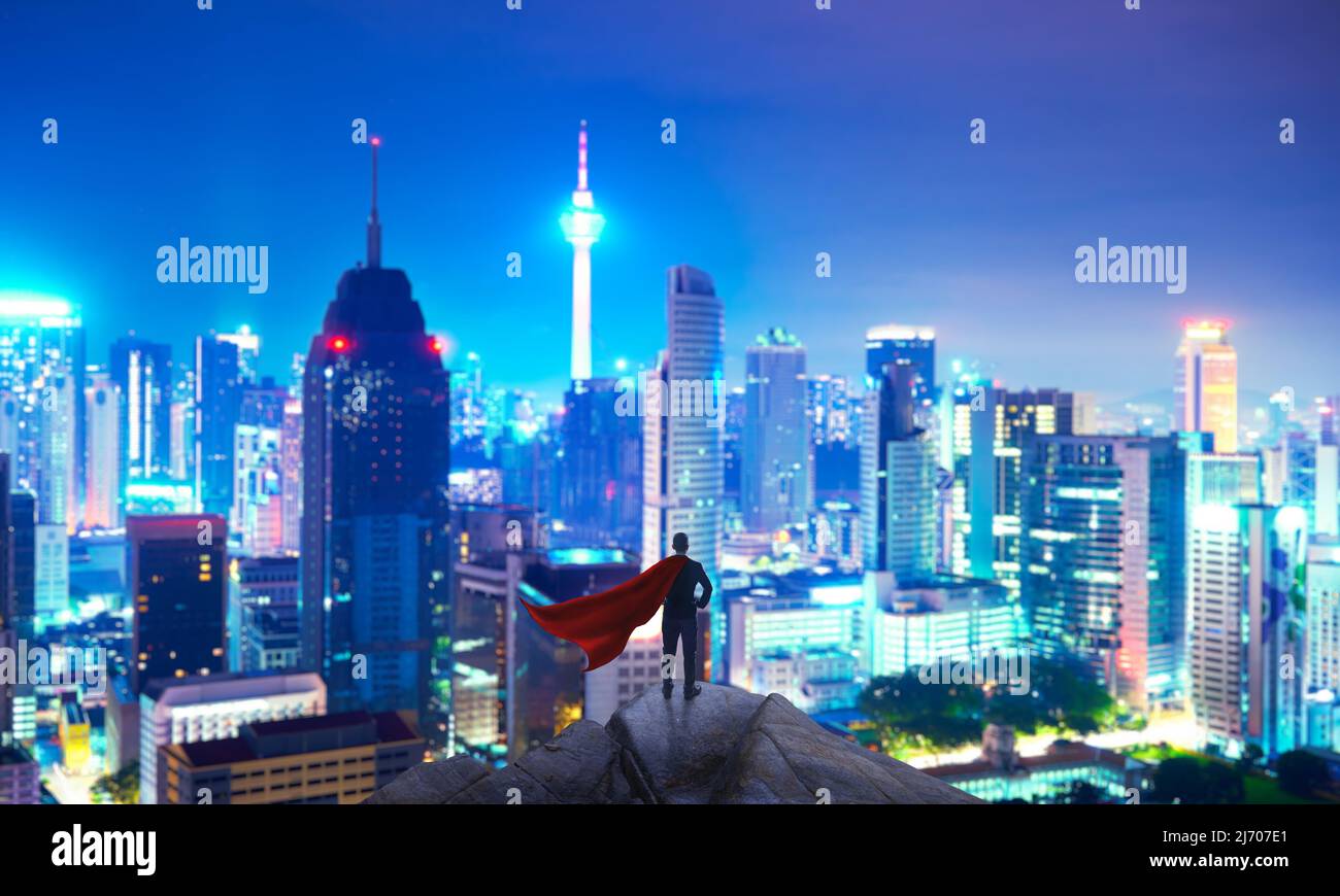 Geschäftsmann in Anzug und Umhang Held stehen oben mit Blick auf die Stadt und denken Business-Plan der Zukunft . Nachtaufnahme . Stockfoto