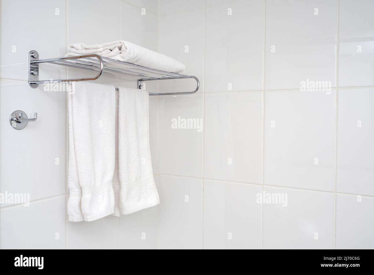 Die Innenausstattung des Badezimmers mit Eisenablage und weichen Handtüchern. Weiße Fliesen mit minimaler Zusammensetzung im Badezimmer. Stockfoto
