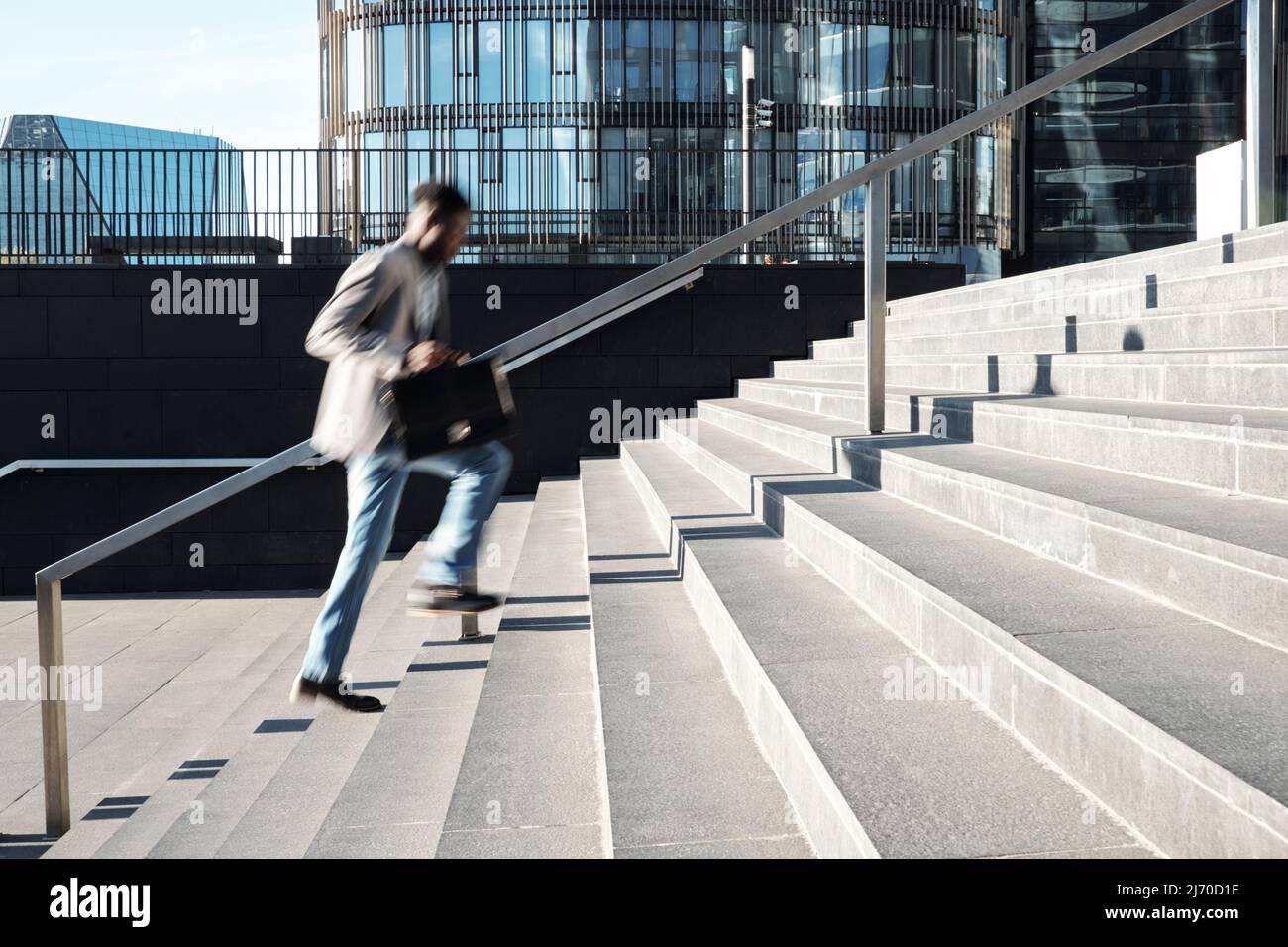 Afroamerikanische Angestellte, die die Stufen in Richtung eines modernen Geschäftszentrums hochlaufen, verschwommene Bewegungen Stockfoto