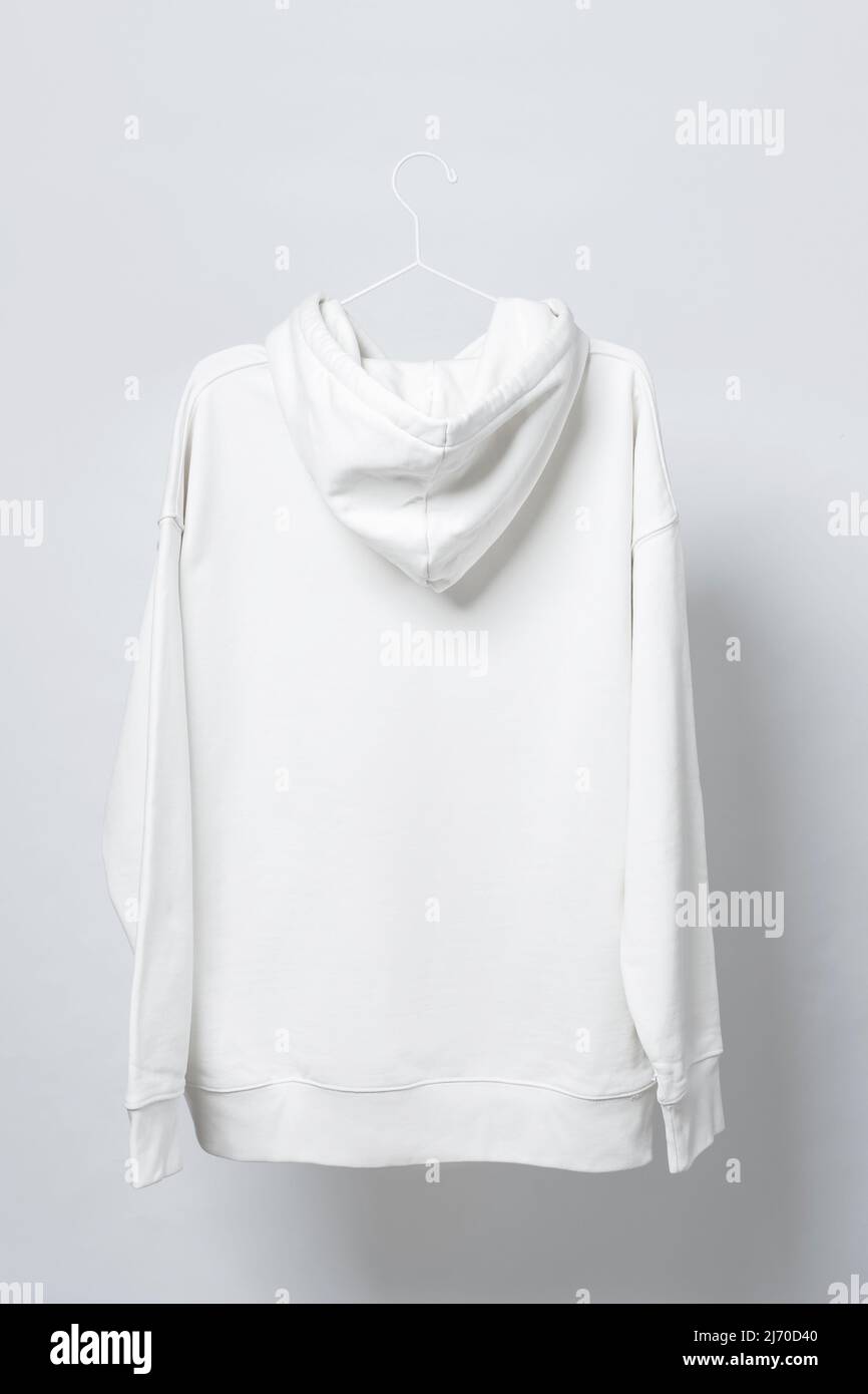 Ein leerer weißer Hoodie hängt vor grauem Hintergrund an einem Kleiderbügel Stockfoto