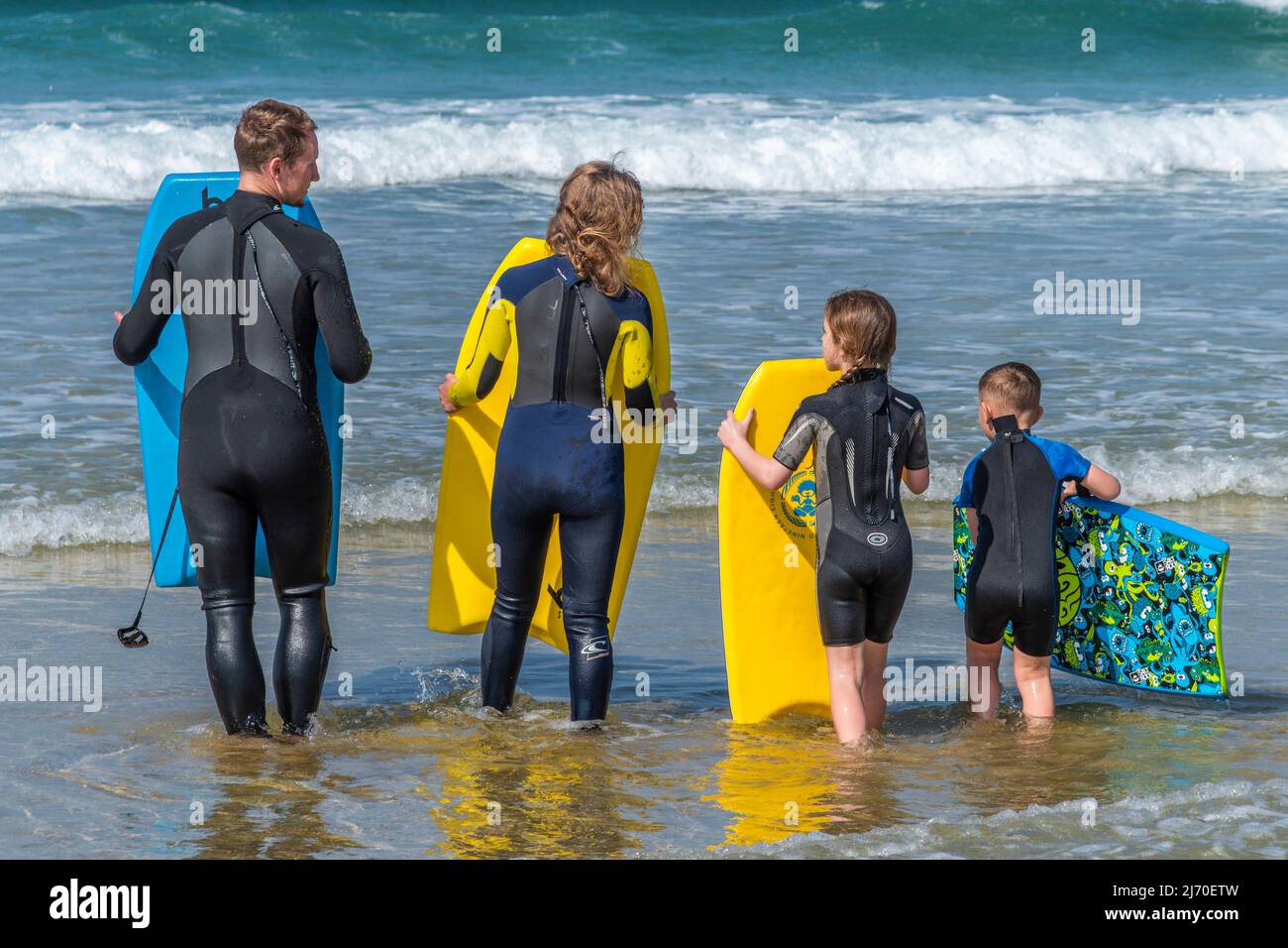 Eine junge Familie von Urlaubern, die das für die Jahreszeit unangenehme warme Wetter mit ihren Bodyboards im Meer am Fistral Beach in Newquay genießen. Stockfoto