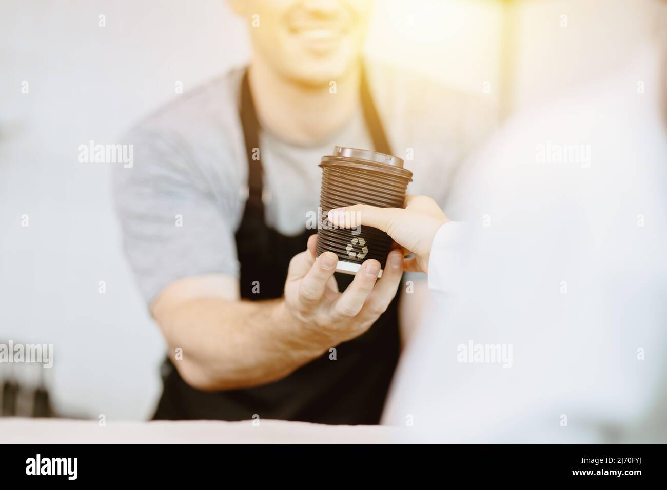 Barista serviert dem Gast heiße Getränke mit einem Becher aus recyceltem Papier Stockfoto