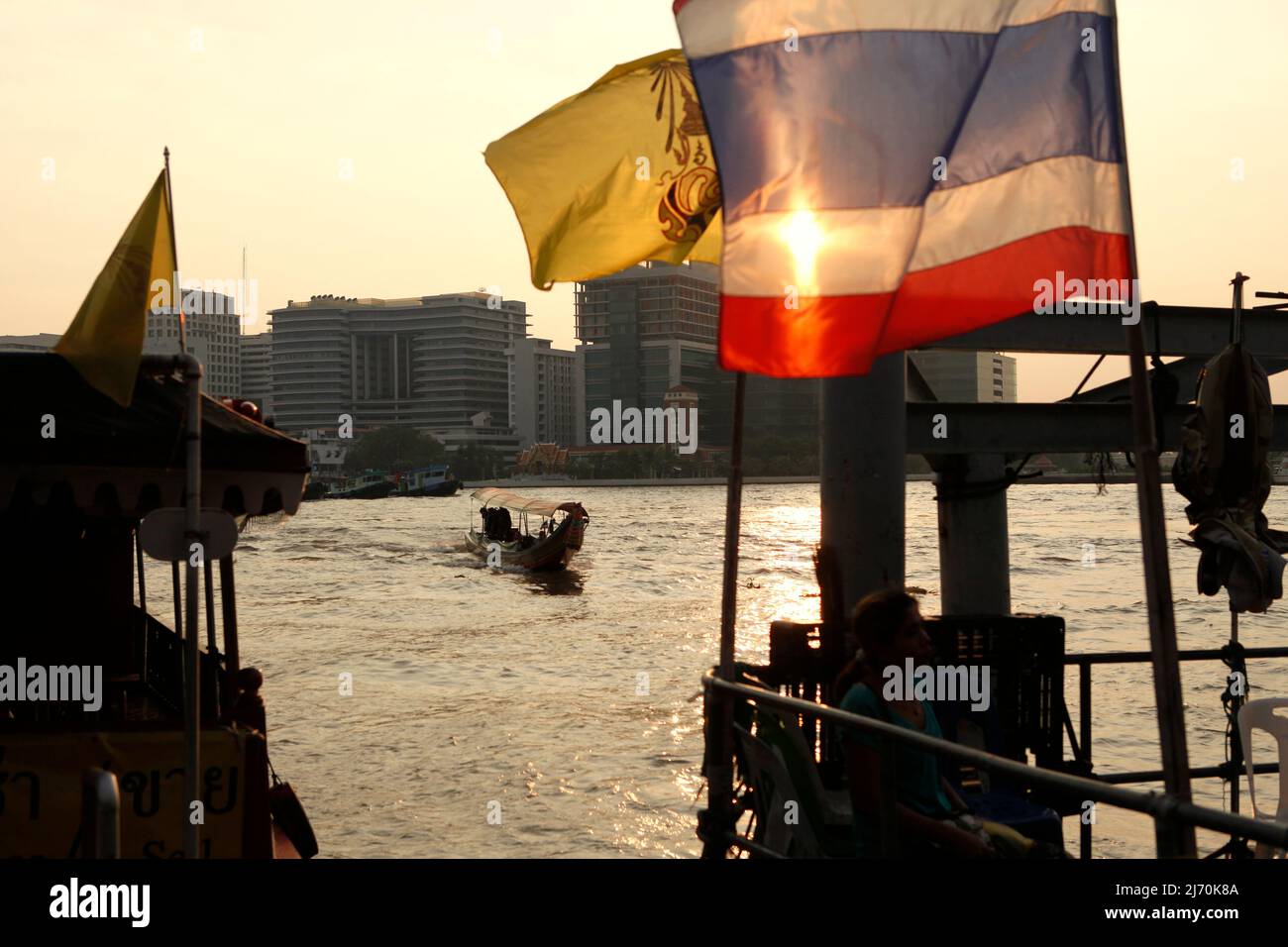 Ein Tourismusboot nähert sich einer Wasserbusstation, die mit einer thailändischen Nationalflagge am Ufer des Chao Phraya Flusses in Bangkok, Thailand, dekoriert ist. Stockfoto