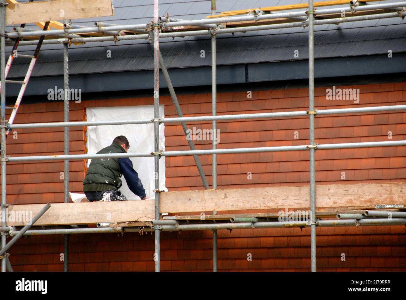 Arbeiter, der die Fensteröffnung in einem im Bau befindlichen Haus als Vorsichtsmaßnahme gegen schlechtes Wetter abdeckt Stockfoto