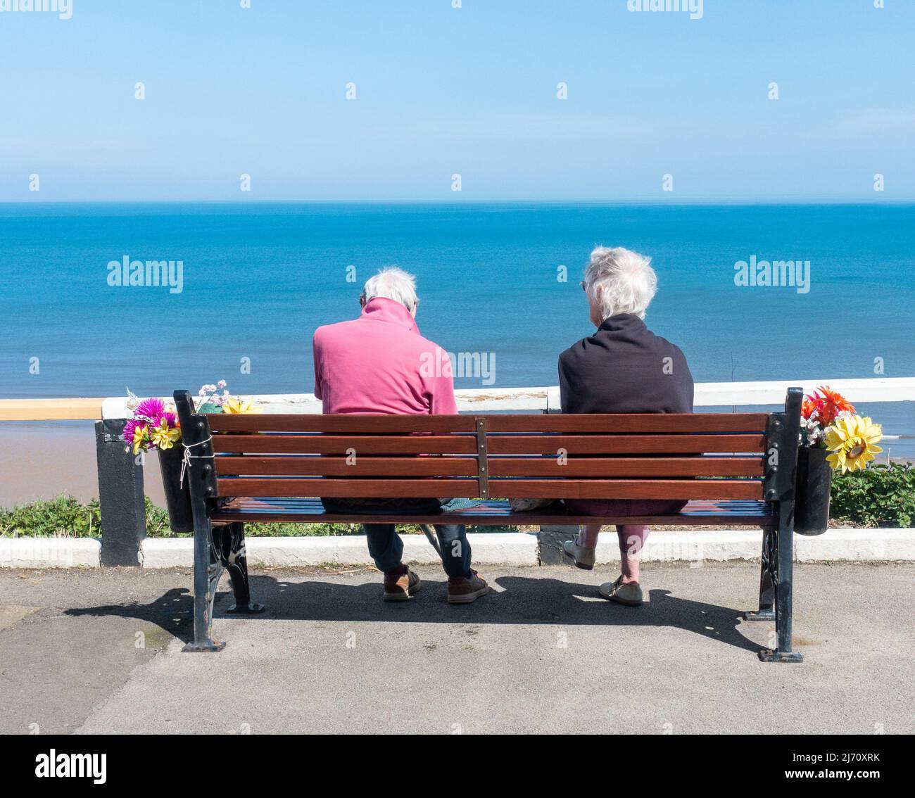 Rückansicht eines älteren Paares, das auf dem Sitz, der Bank, mit Blick auf das Meer von der oberen Promenade in Saltburn am Meer sitzt. VEREINIGTES KÖNIGREICH Stockfoto