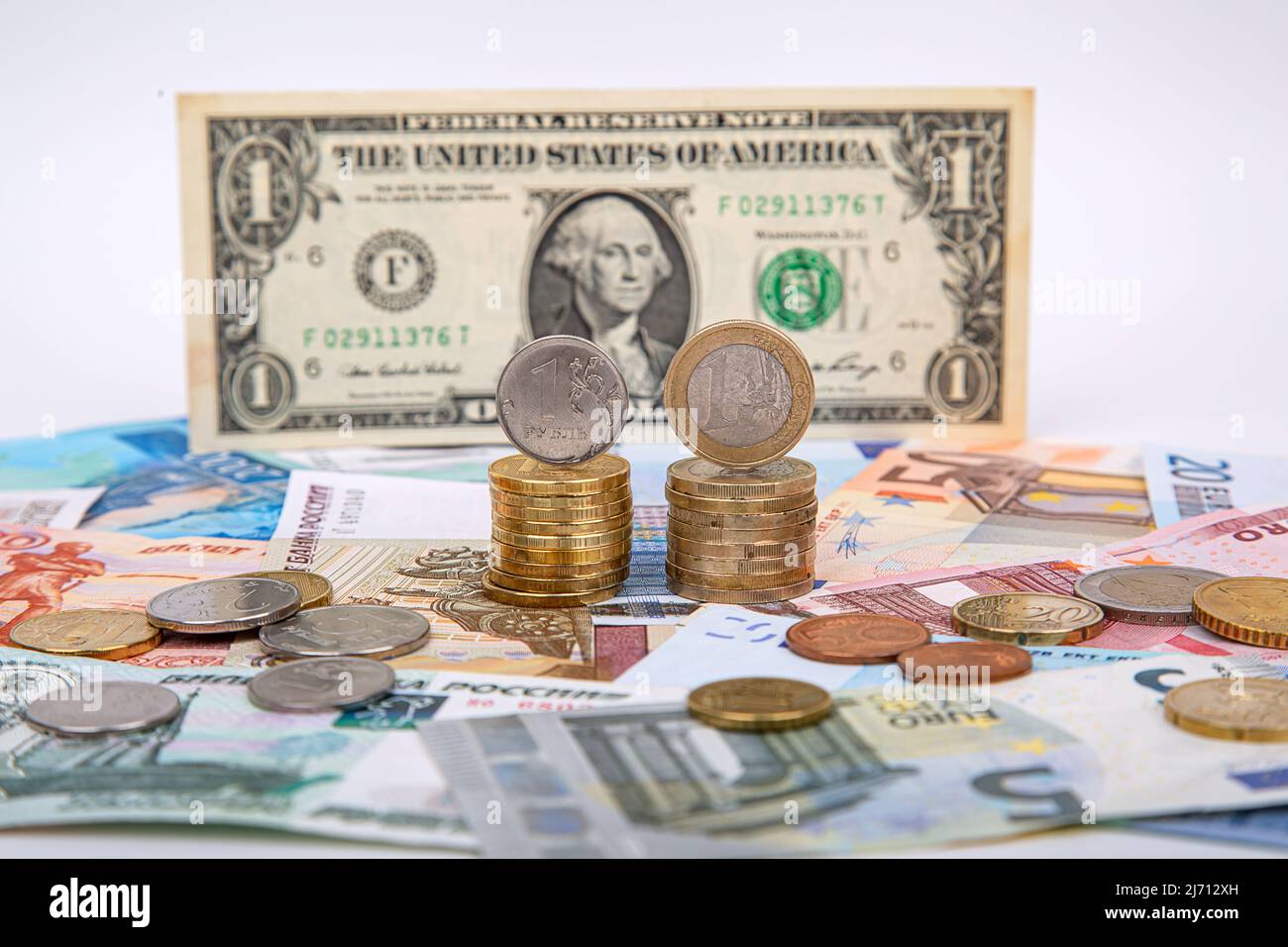 Rubel und Euro gegenüber dem Dollar. Ein Stapel von Rubel-Münzen und Euro-Münzen auf dem Hintergrund eines US-Dollars Stockfoto