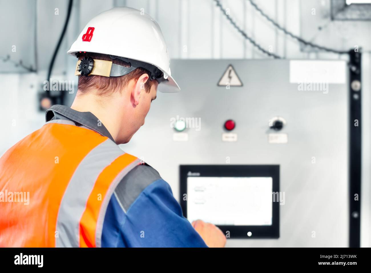 Ingenieur im Helm schaut sich den Monitor an und programmiert die Ausrüstung. Automatisierung der Arbeit in der Produktion. Echte Workflow-Szene. Stockfoto