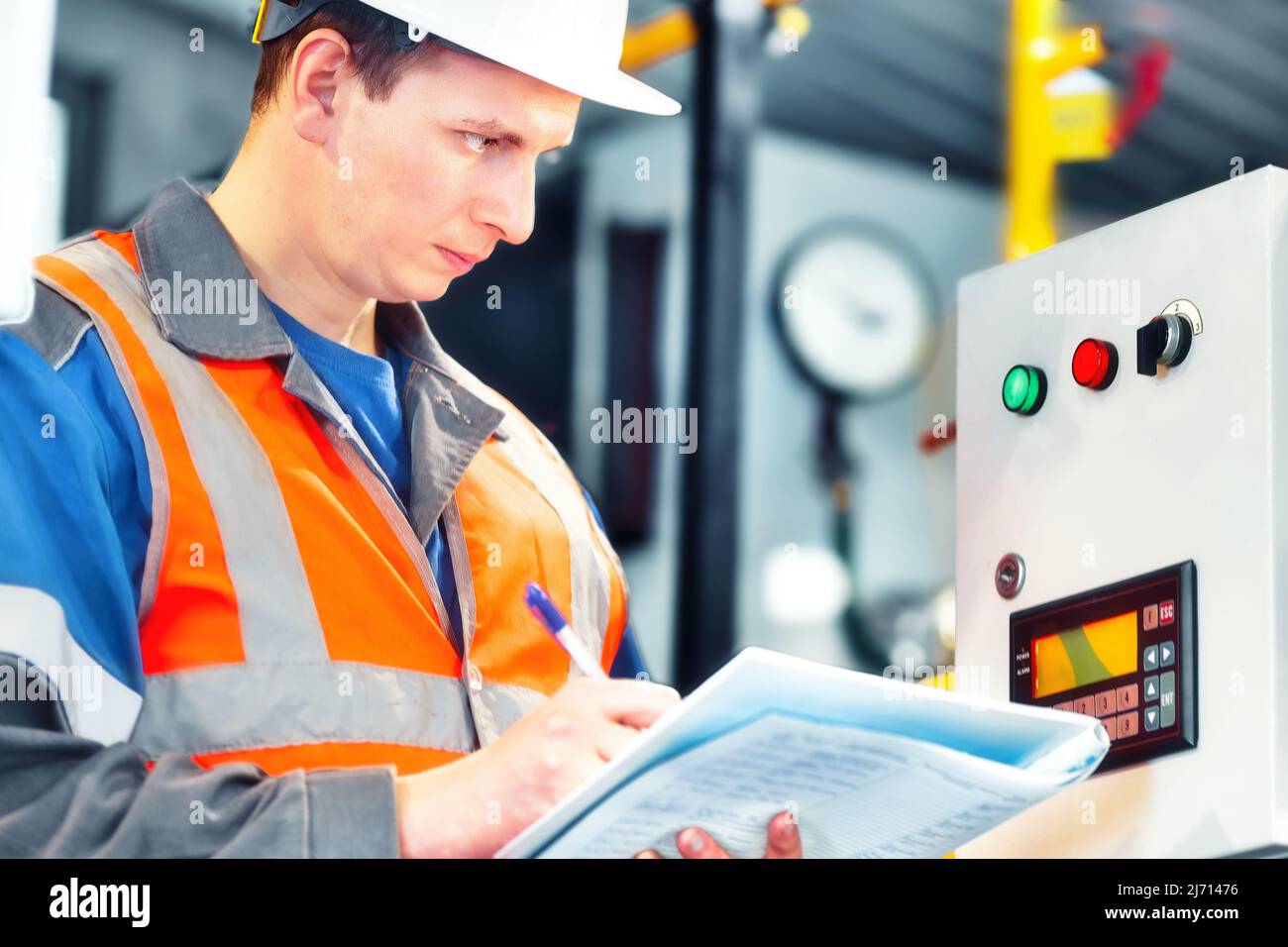 Der junge Ingenieur, der Helm und Schutzweste verwendet, zeichnet die Messwerte der Geräte oder des Gasverbrauchs im Kesselraum auf. Beginn der Heizperiode und Gasversorgung. Stockfoto