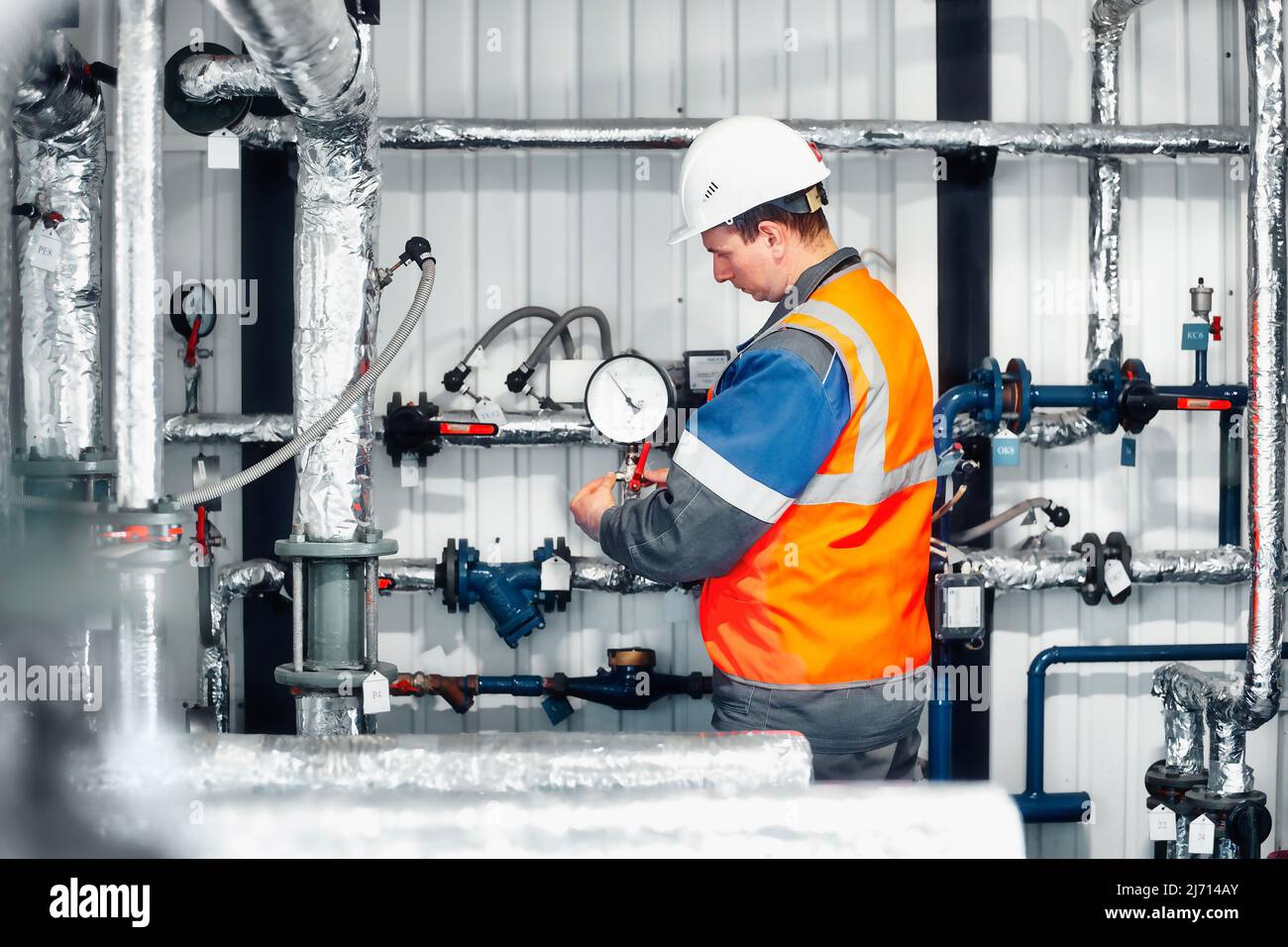 Der Betreiber des Gaskesselhauses in Helm und Schutzweste überprüft die Druckwerte der Druckmessgeräte in der Produktionsanlage. Vorbereitung von Anlagen und Geräten für die Heizperiode. Gasversorgung nach Europa. Stockfoto
