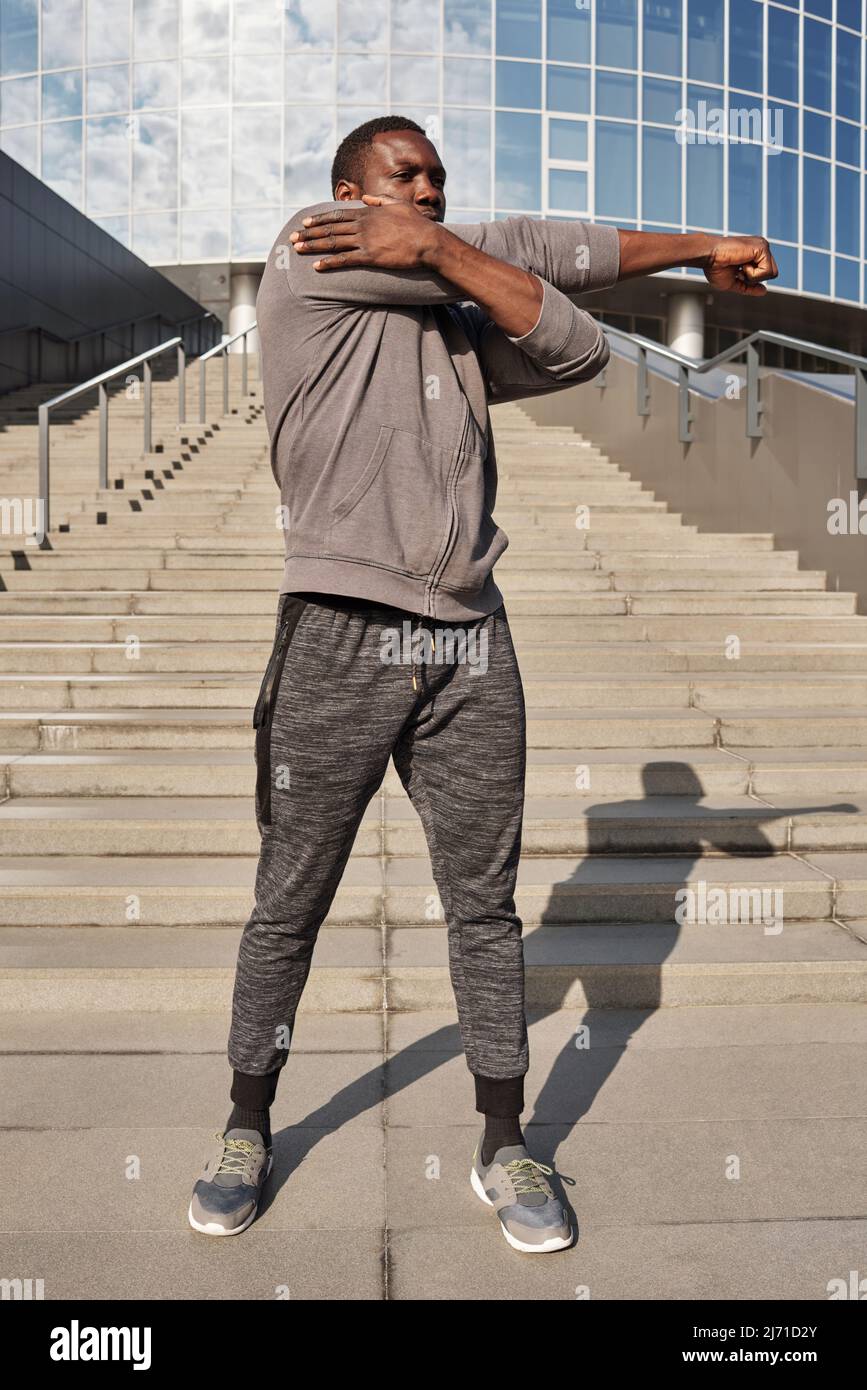 Der junge afroamerikanische Sportler im aktiven Sport macht Aufwärmübungen, während er im Freien vor dem modernen Business Center steht Stockfoto