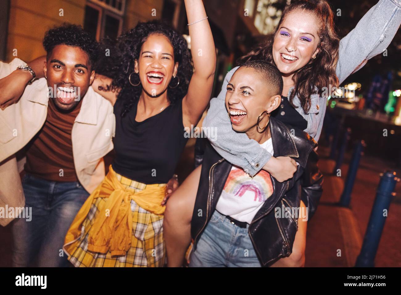 Gruppe von Freunden, die lachen und ihr bestes Leben in der Stadt leben. Fröhliche junge Leute, die Spaß haben, während sie abends zusammen abhängen. Lebendige Freunde Stockfoto