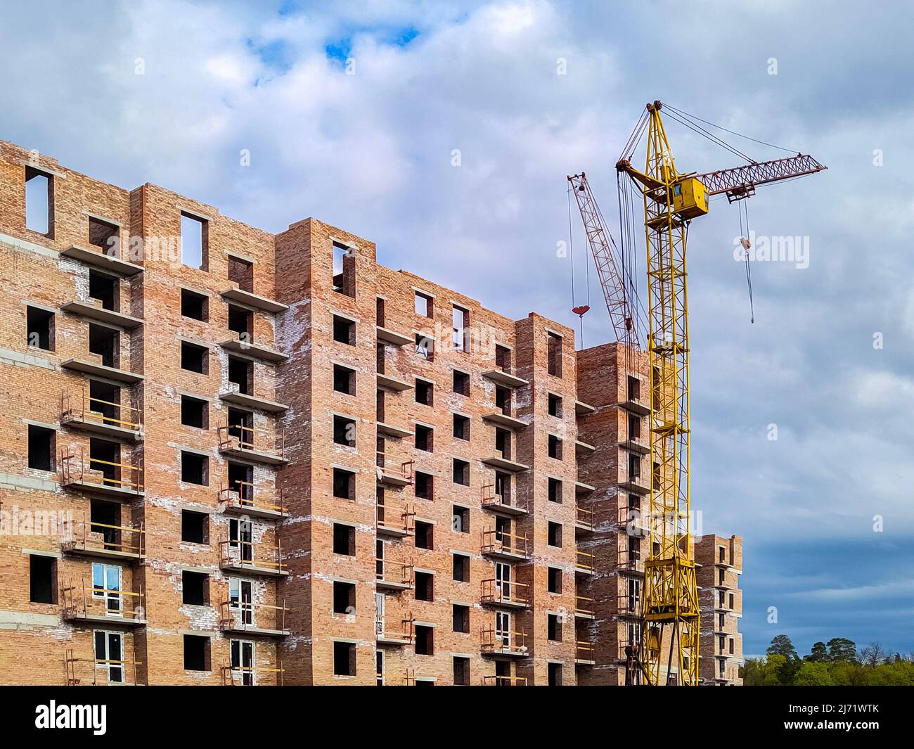 Wohnhaus aus Backstein im Bau. Unvollendetes Haus und Turmdrehkran. Neues mehrstöckiges Gebäude Stockfoto